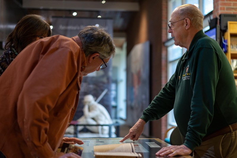 Orientation at the Chancellorsville Battlefield Visitor Center A middle aged couple stand at a visitor center desk and speak with a park service volunteer.