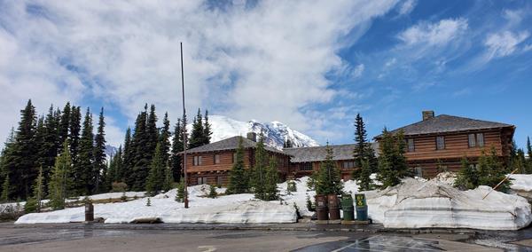 Three rustic wooden buildings sit on rise with snow and ice covered Mount Rainier in the background.