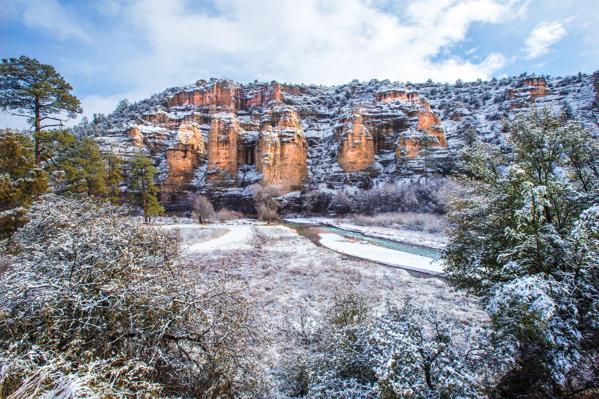 Light snowfall on red rock cliffs along river.