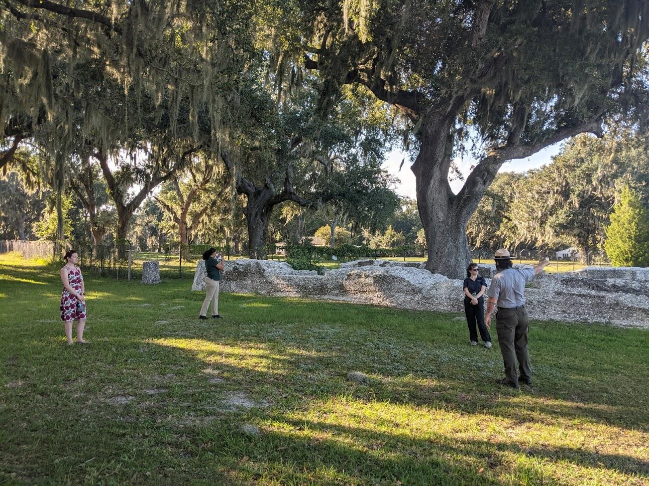 A Park Ranger points at the ruins of a tabby wall with three people looking on