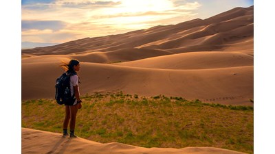 Girl with backpack viewing dunes at sunset