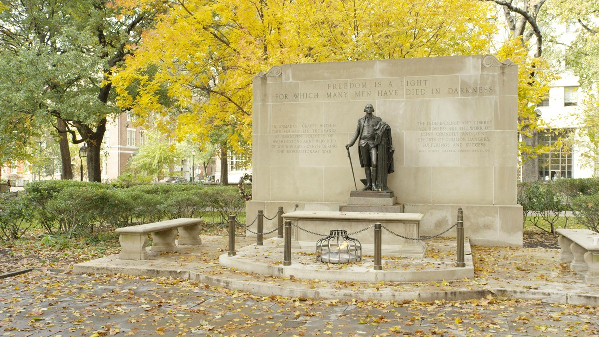 Bronze statue of George Washington standing over a tomb with an eternal flame .