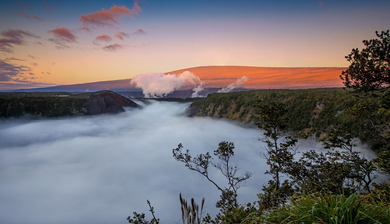 Kīlauea Iki A cloud-filled volcanic crater at sunrise with a mountain rising behind