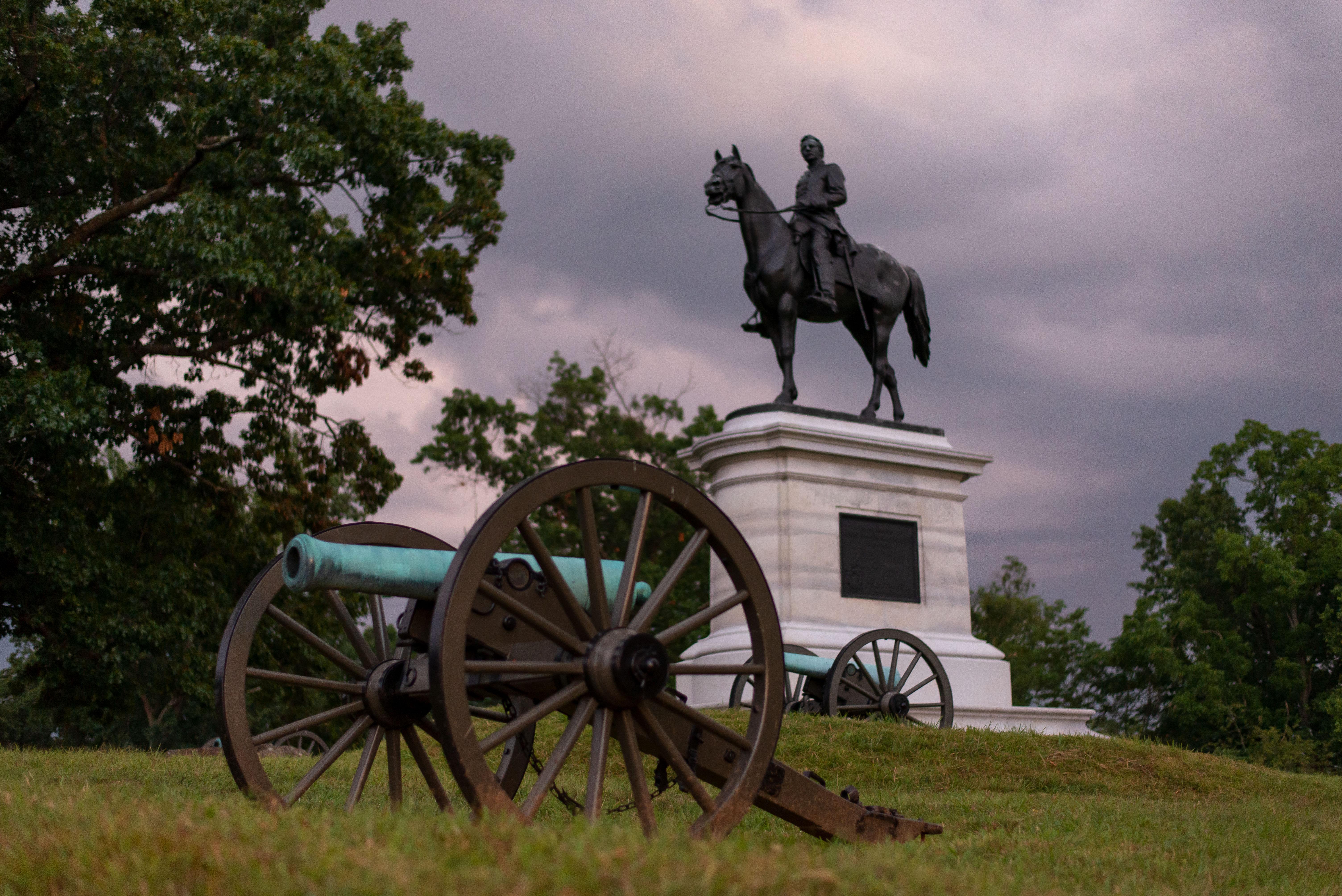 A canon sits in front of an equestrian statue.