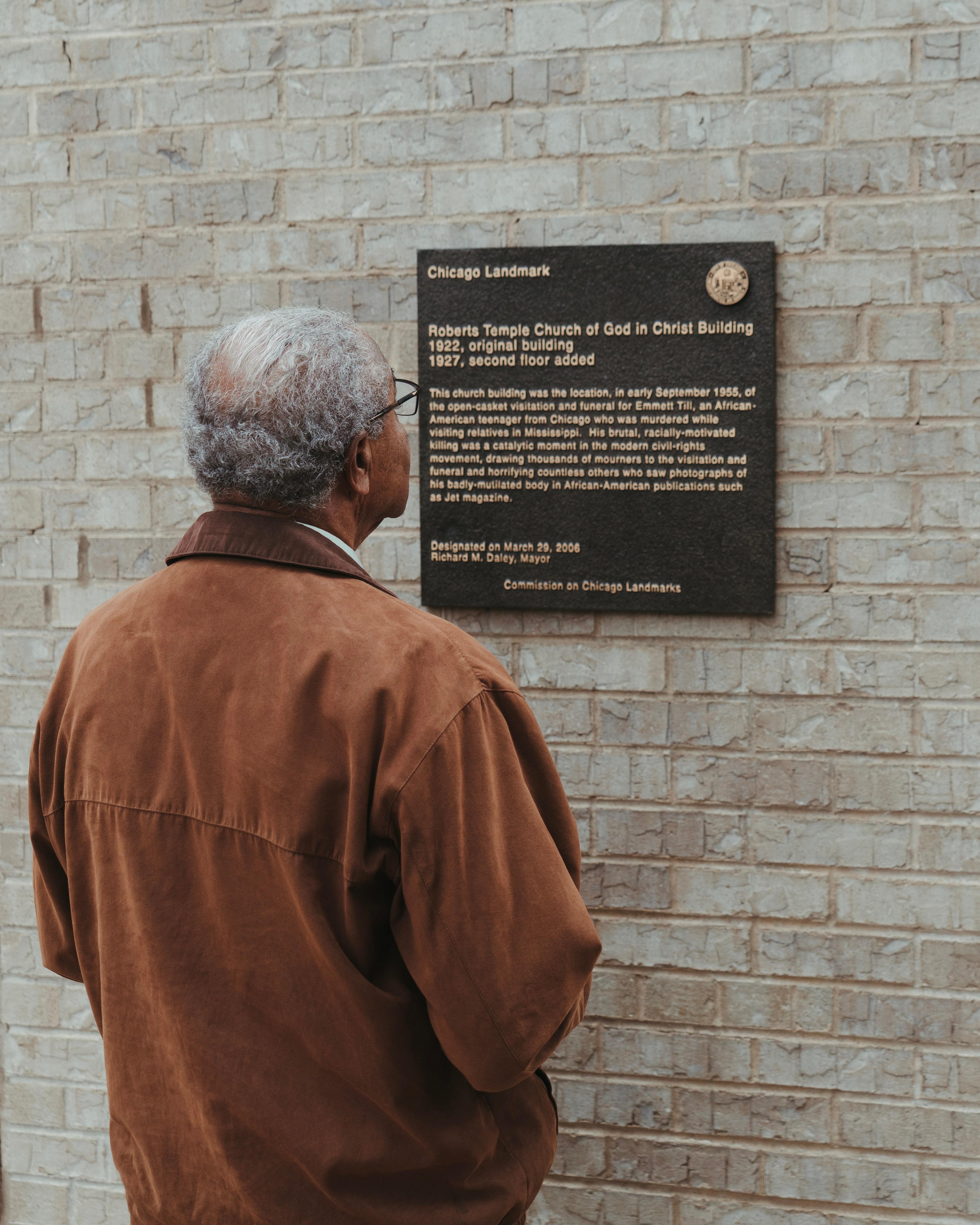 An elderly African American man looks at a plaque on the church exterior.