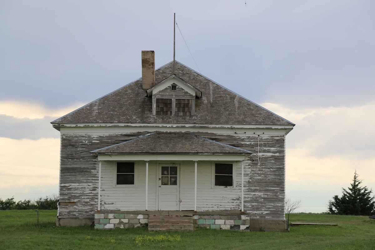 Frame one story schoolhouse with most of white paint worn off to show gray. 