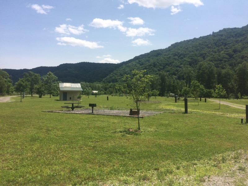 open grassy field with campsites and a composting restroom facility in it