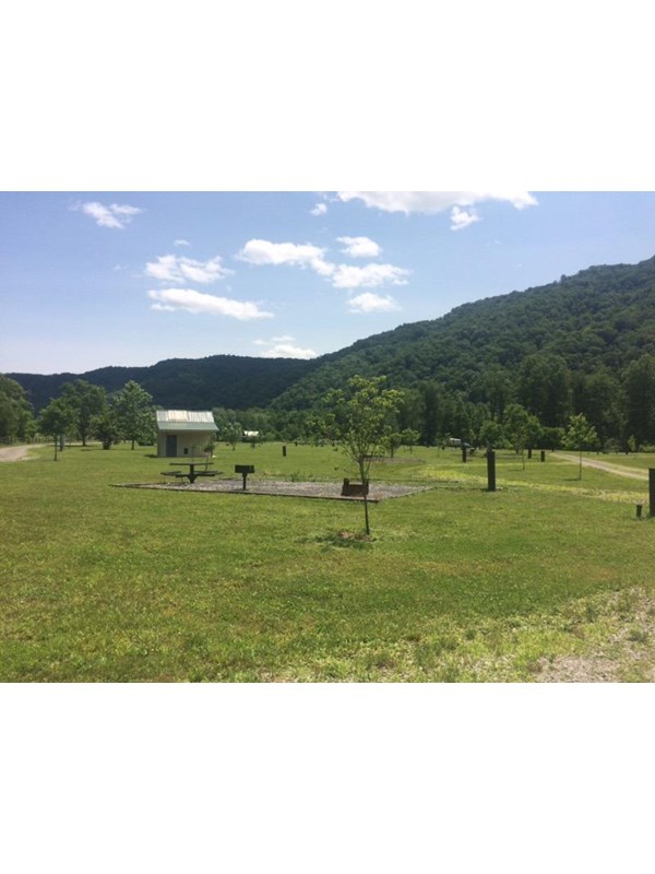 open grassy field with campsites and a composting restroom facility in it