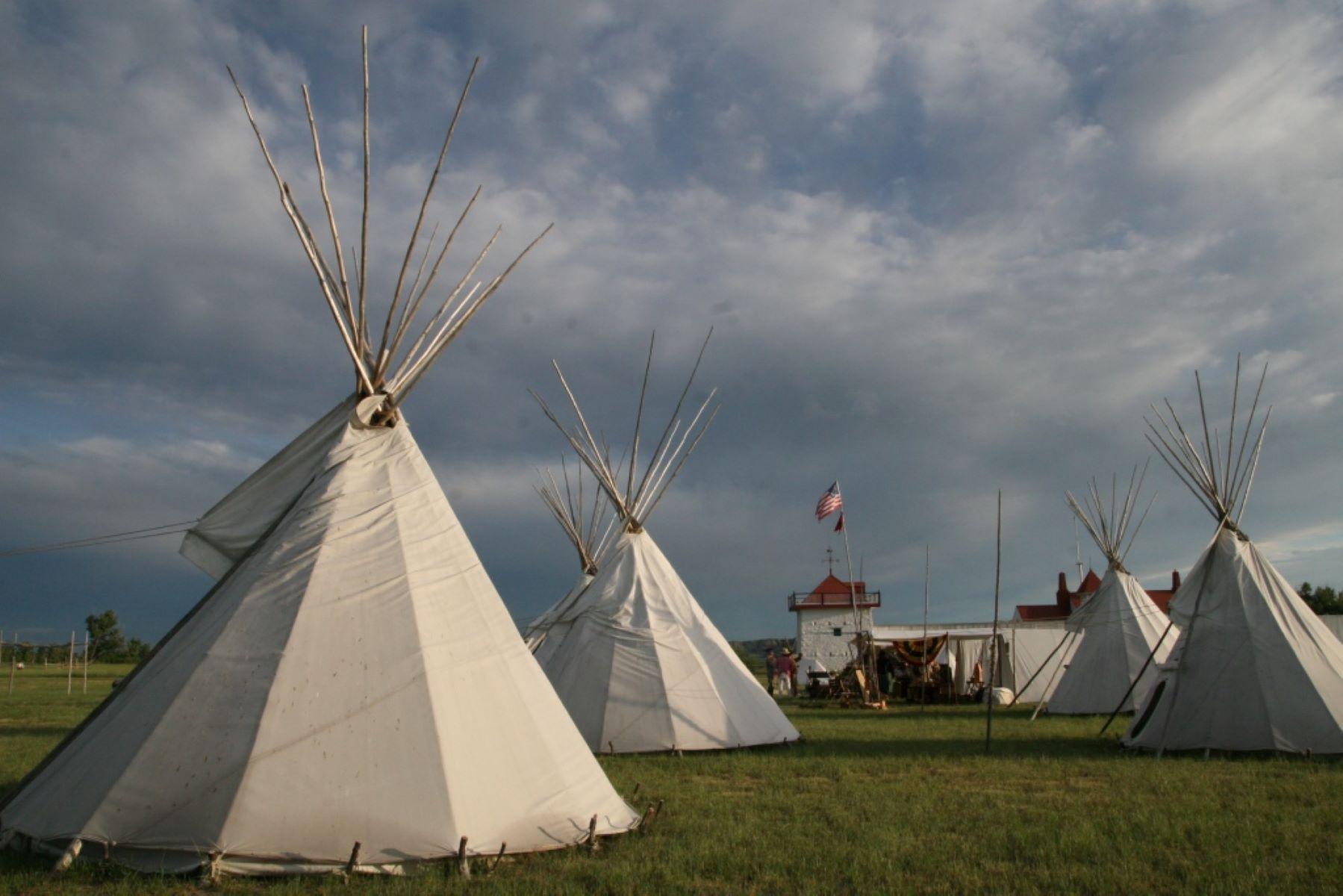 White canvas tipis in grassy area, Fort in background.