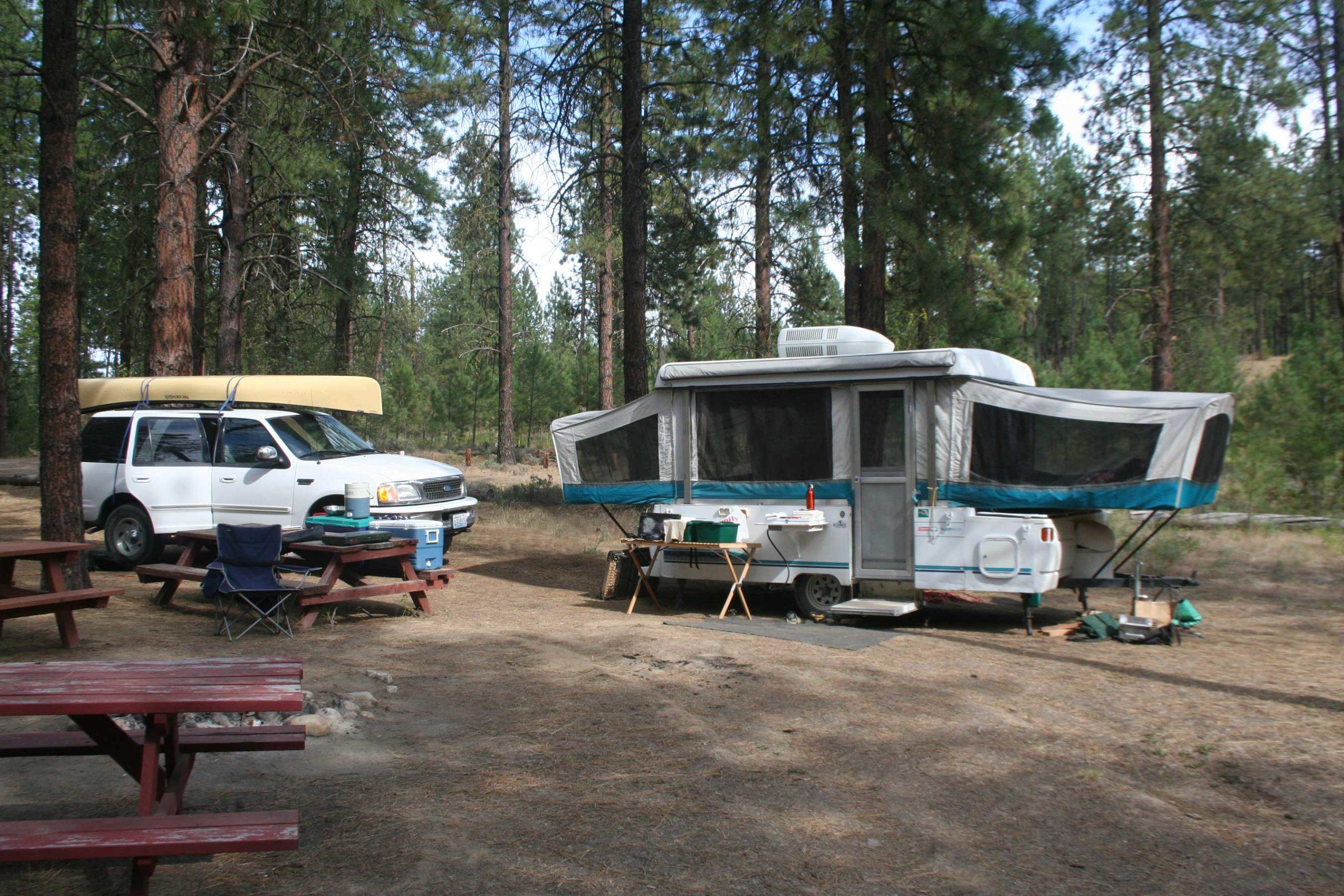 White truck with a yellow canoe is separated from a white camping trailer.