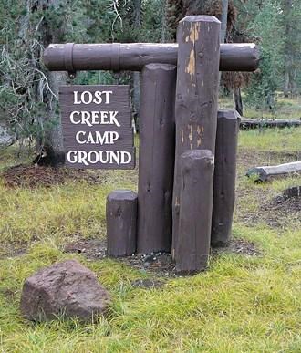 four 8-inch, round, brown, wood posts with a cross beam holding the entrance sign to Lost Creek Camp