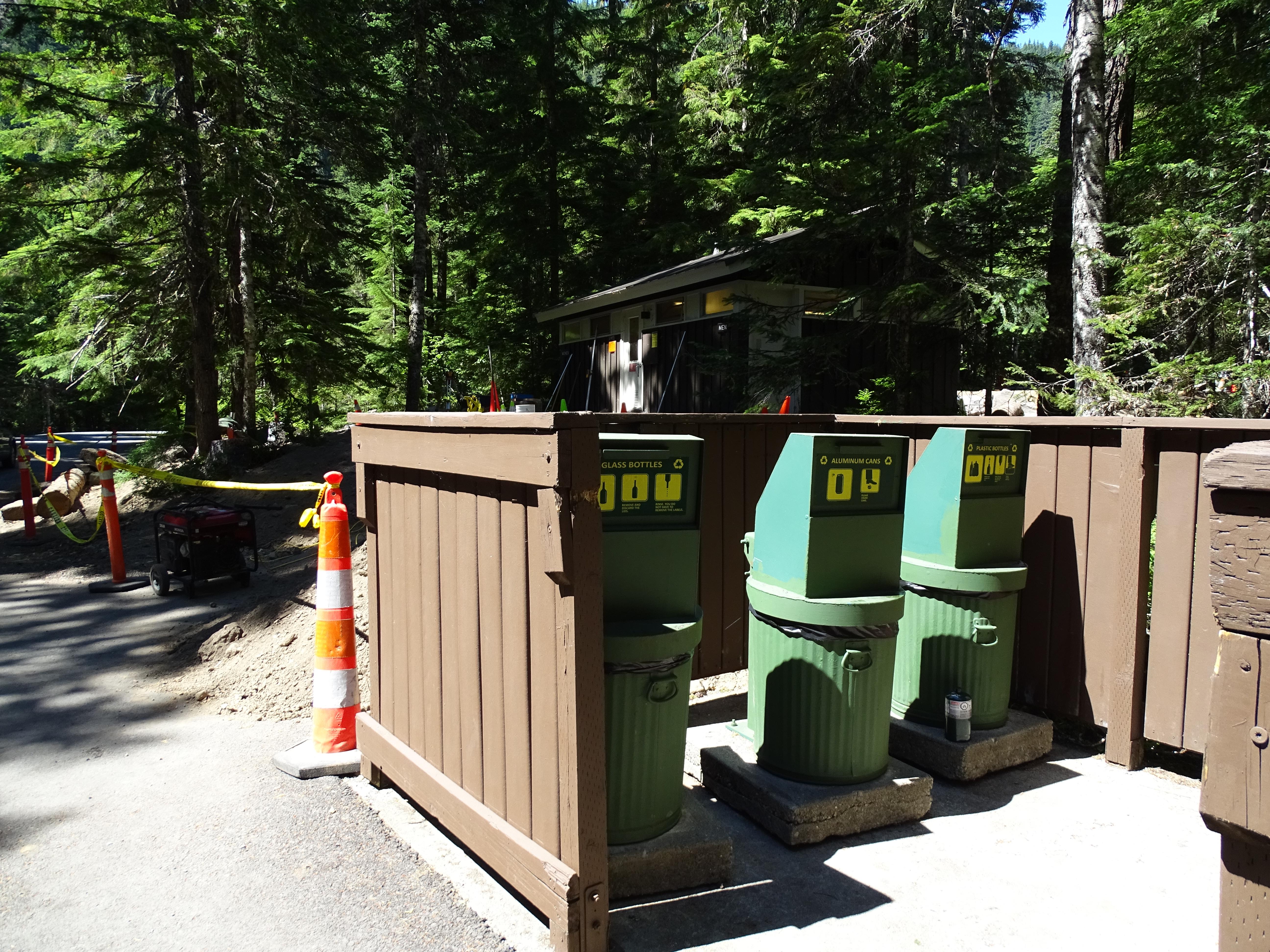 Three green recycling containers inside a wooden enclosure