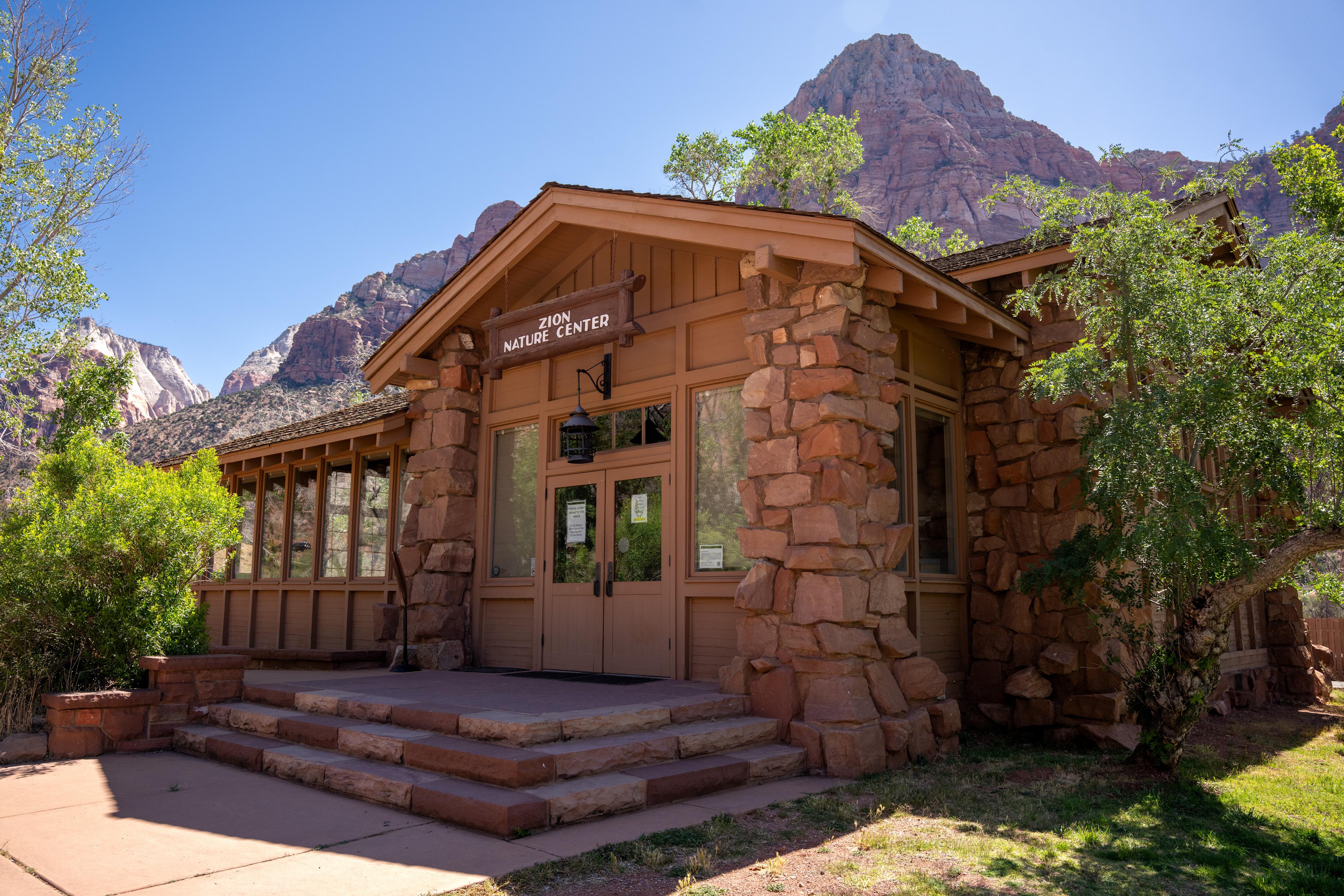 A wood-and-stone building in the bottom of a large sandstone canyon. A sign reads "Nature Center."