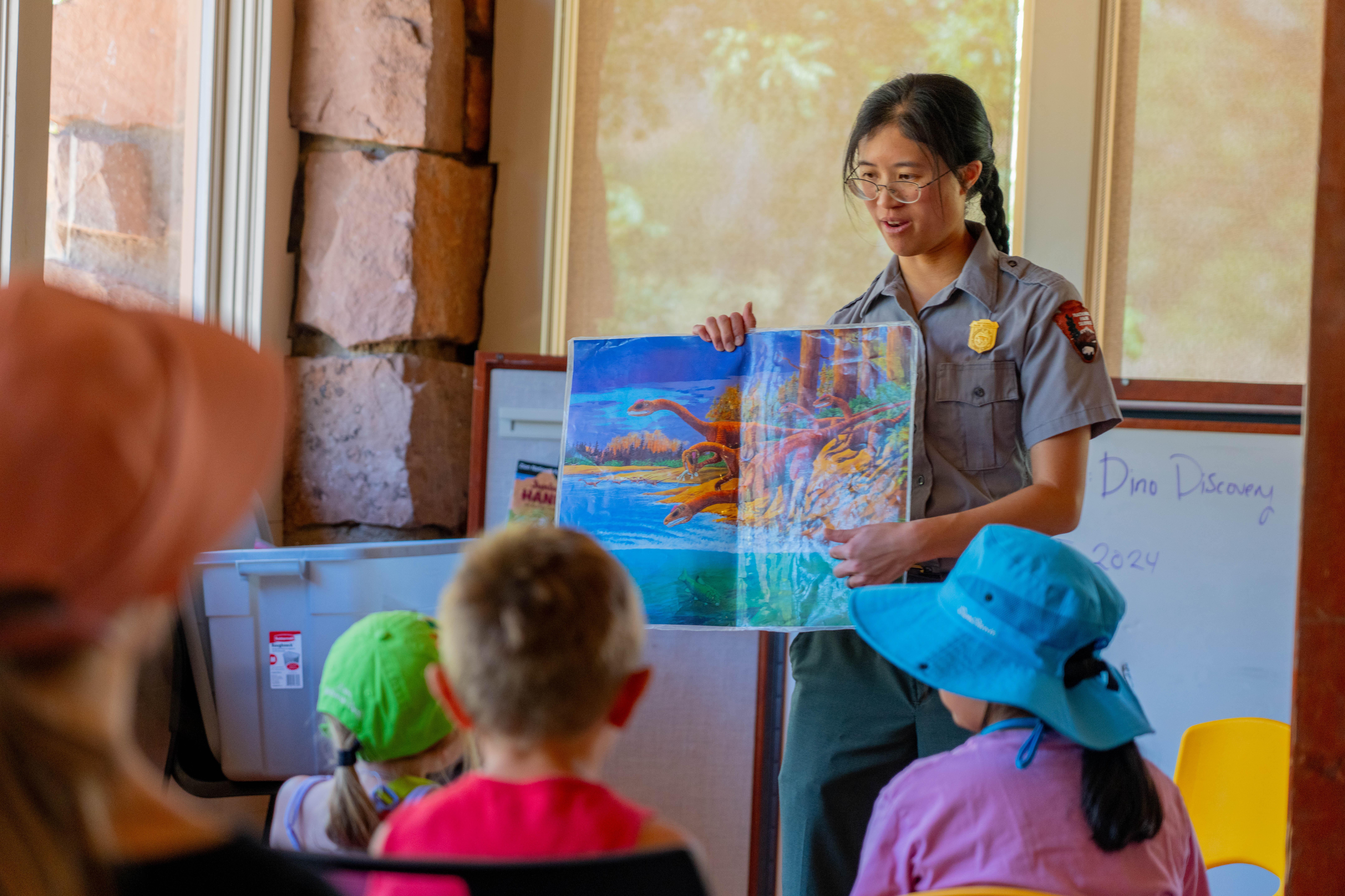 A ranger presents drawings of dinosaurs to a group of children.