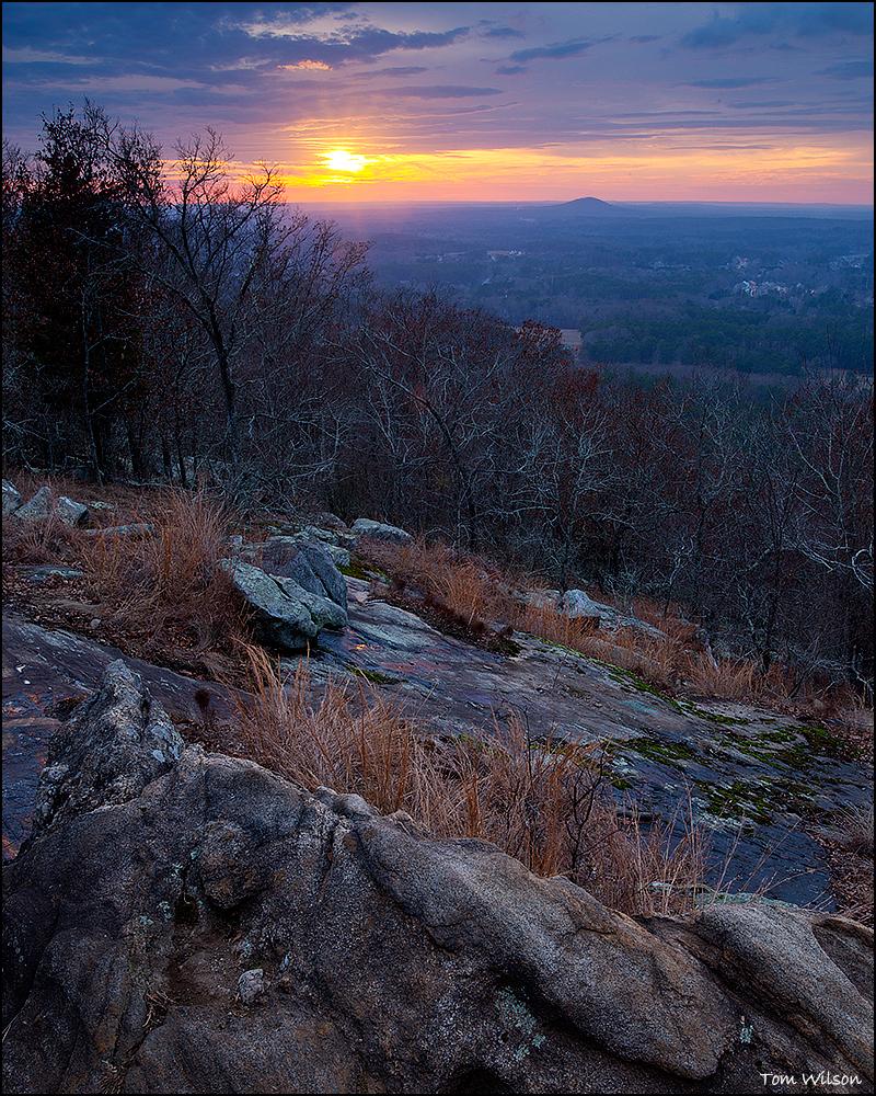 The sun sets in the background with the exposed rock of Kennesaw Mountain in the foreground.