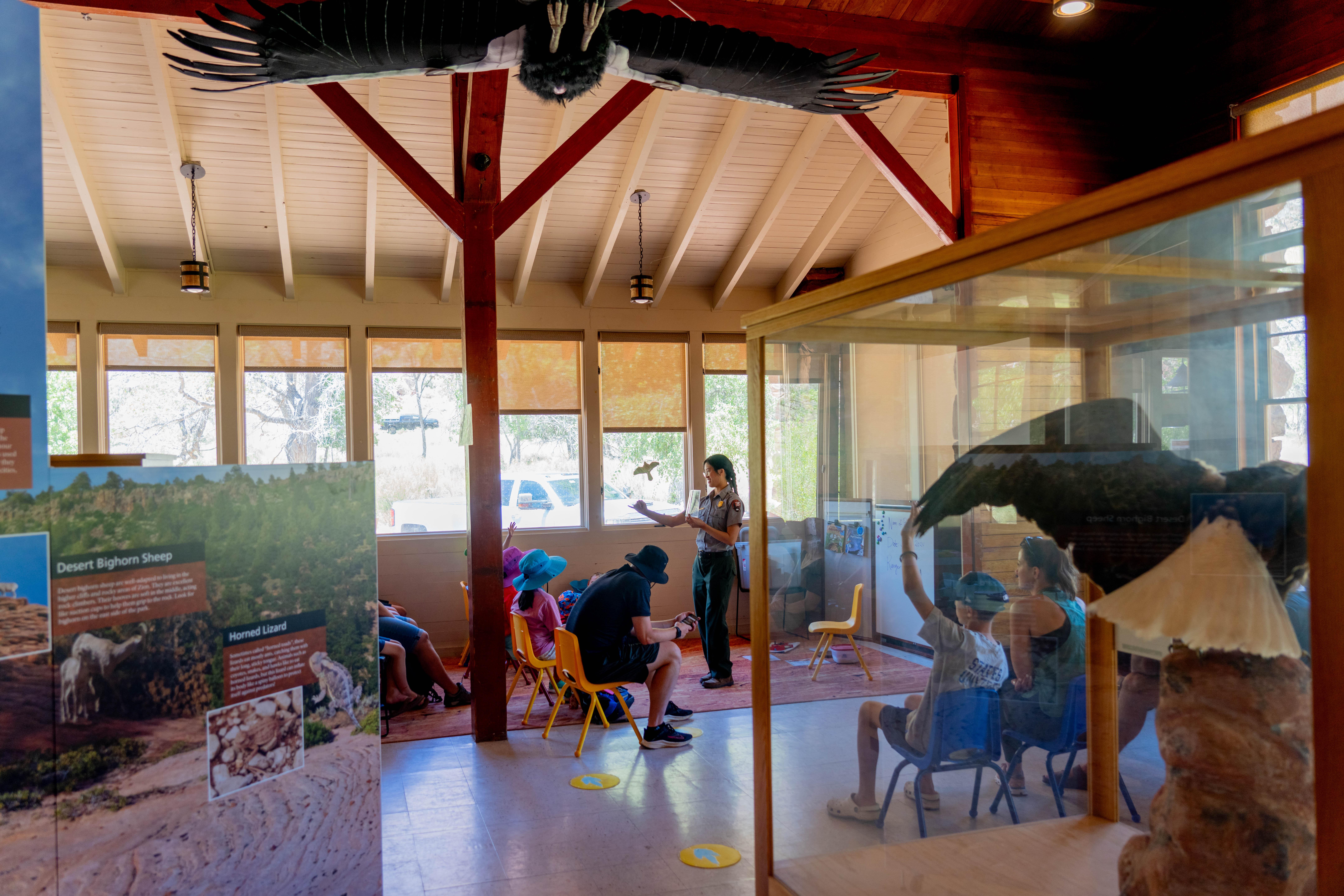 A ranger presents pictures to children and adults. Nearby, there are exhibits about animals.