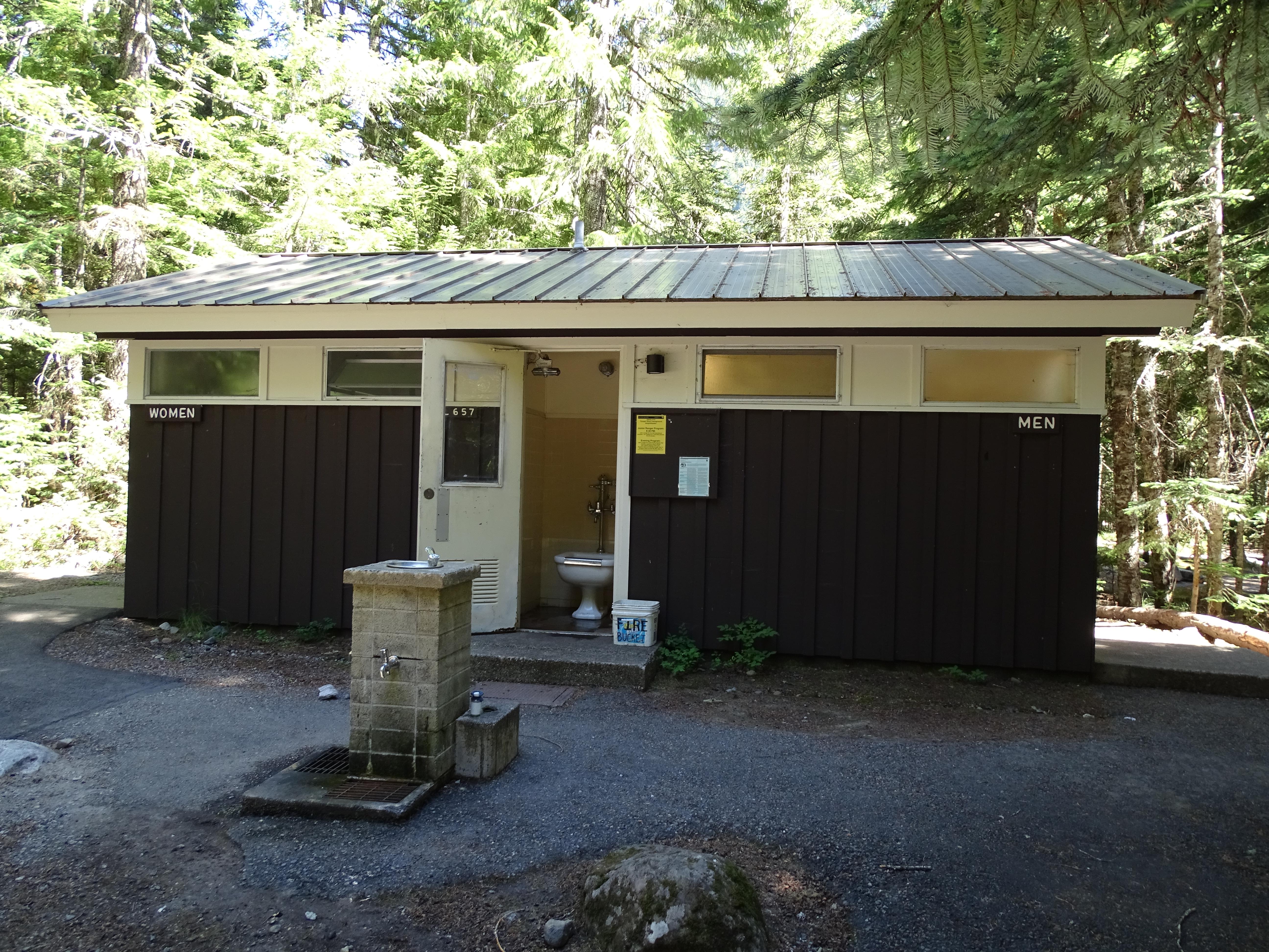 A small brown building with a stone structure for obtaining water in front.