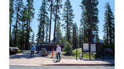Two people walk along a paved pathway toward a small brown building.