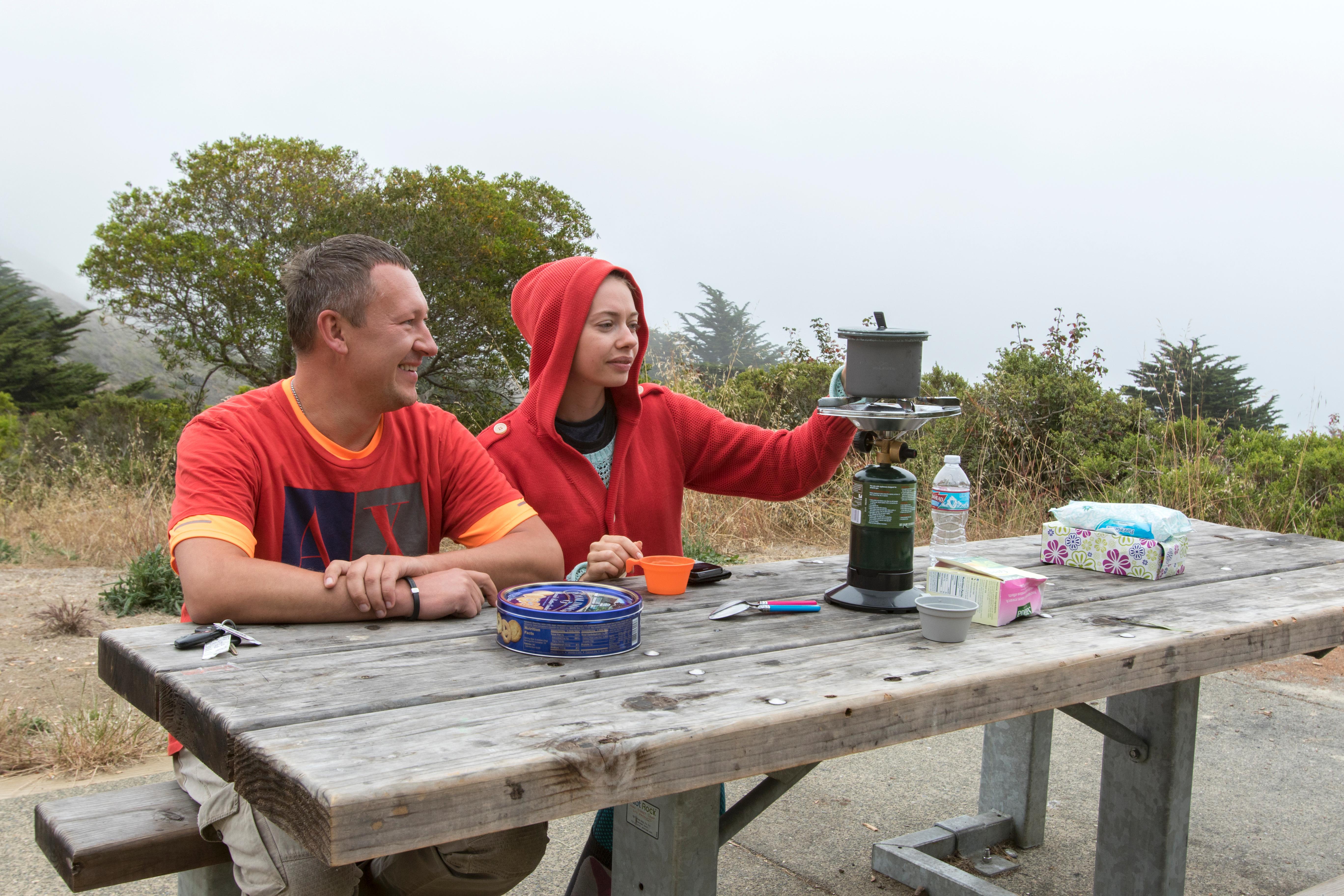 Campers sit contentedly at the picnic table with a gray sky above them.