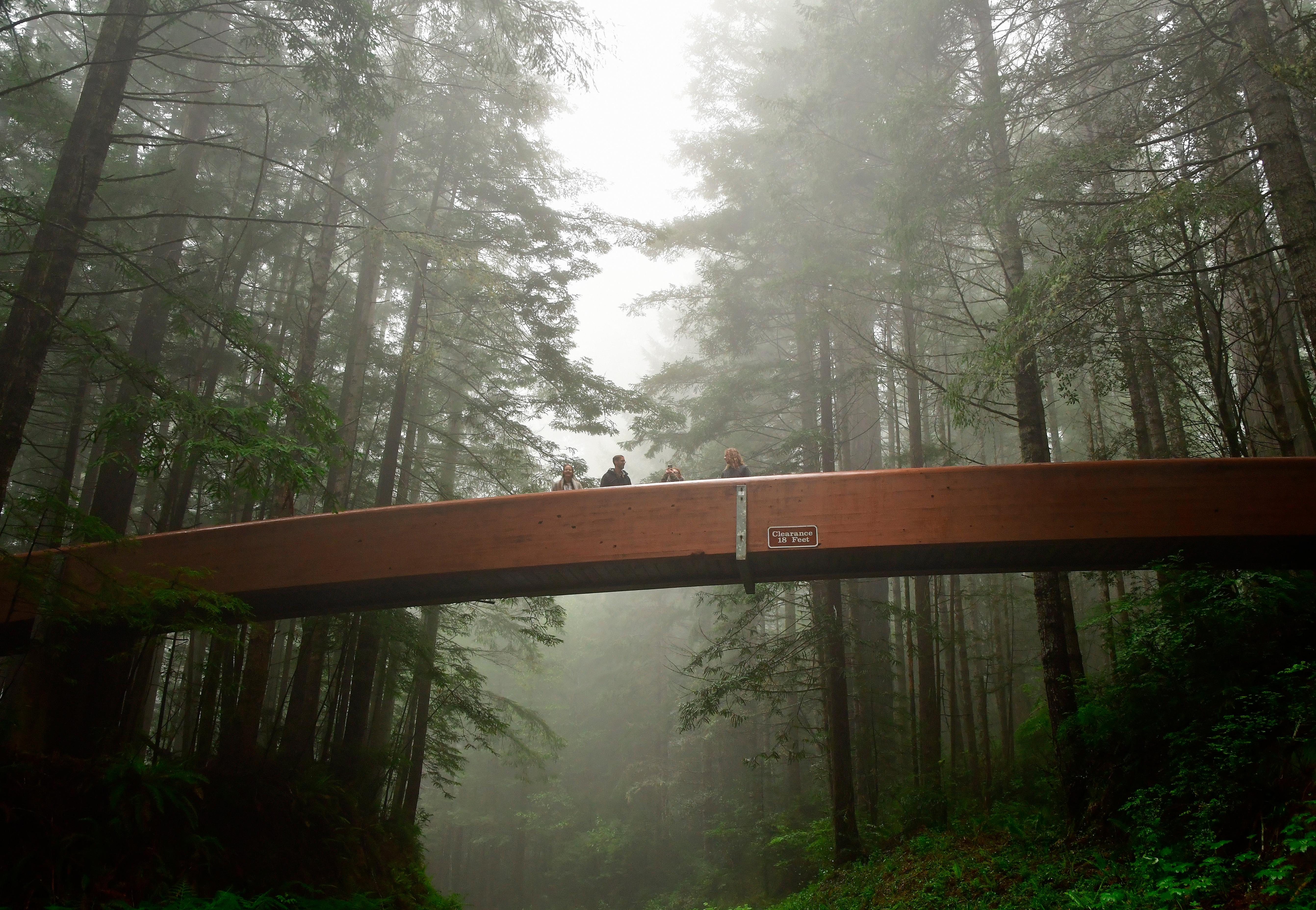A footbridge with people crosses a road on a foggy day