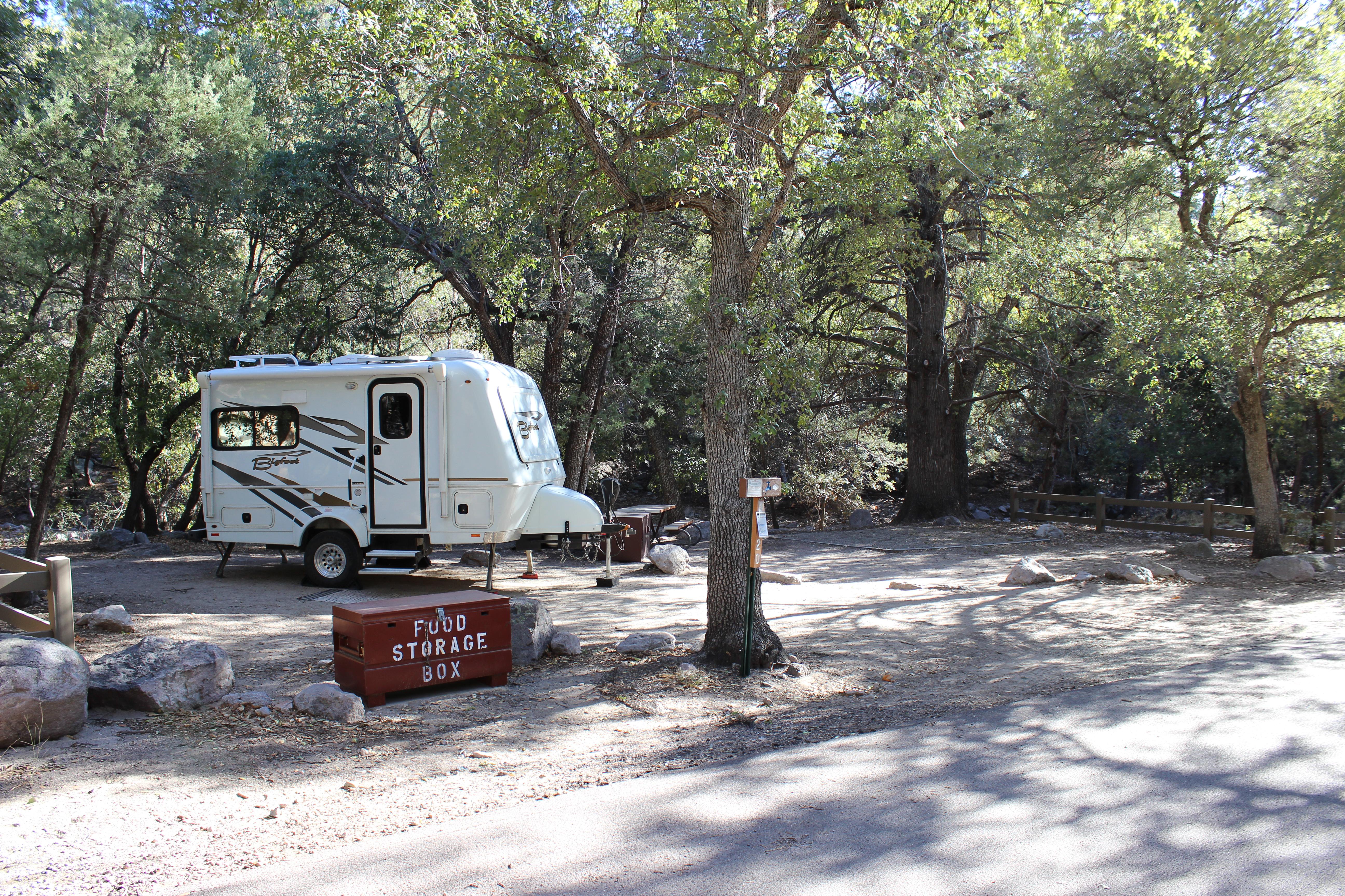 a small trailer is backed into a driveway with a bear box in foreground and trees all around