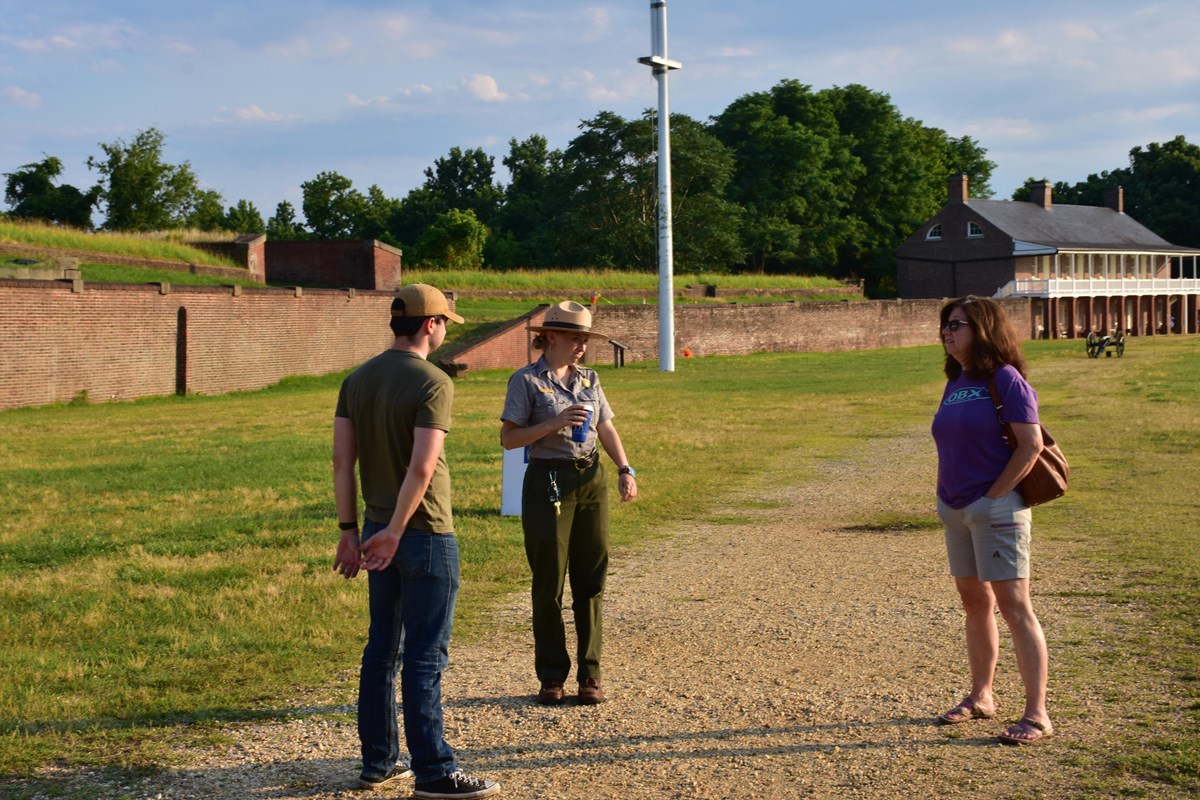 A female park ranger talks with a man and woman in a fort 
