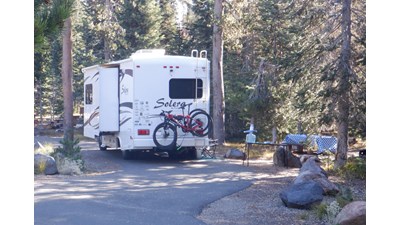 A white Solera RV with one slide out, two bikes on a rack, many stickers from national parks