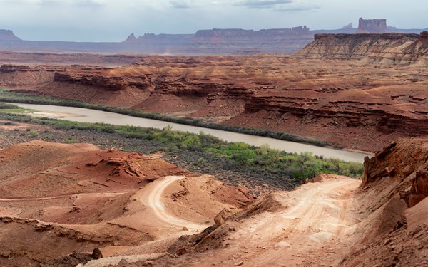 A windy steep dirt road leads up the side of a sandstone cliff. River in background.