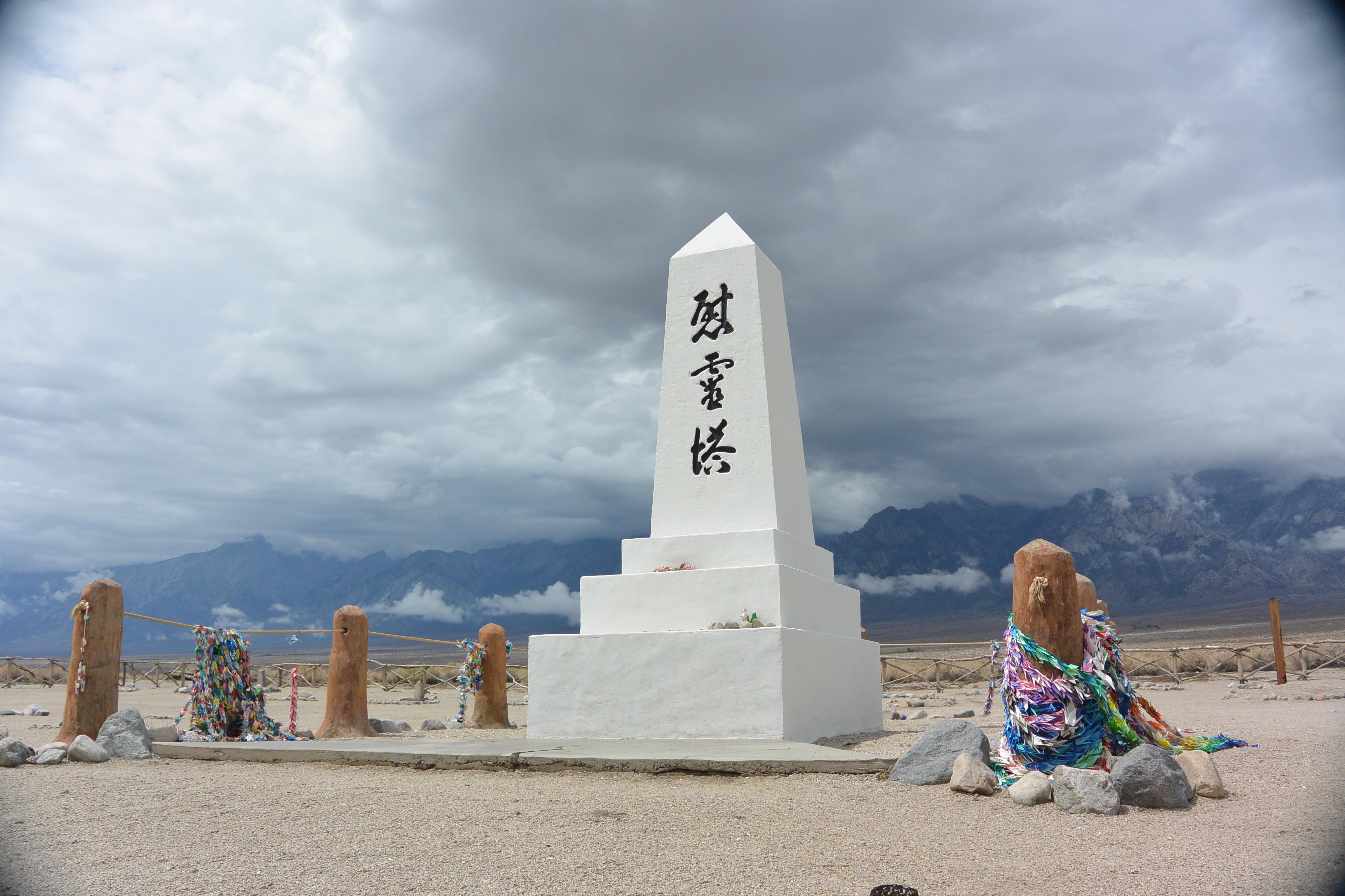 white obelisk with black Japanese characters with stormy mountains beyond
