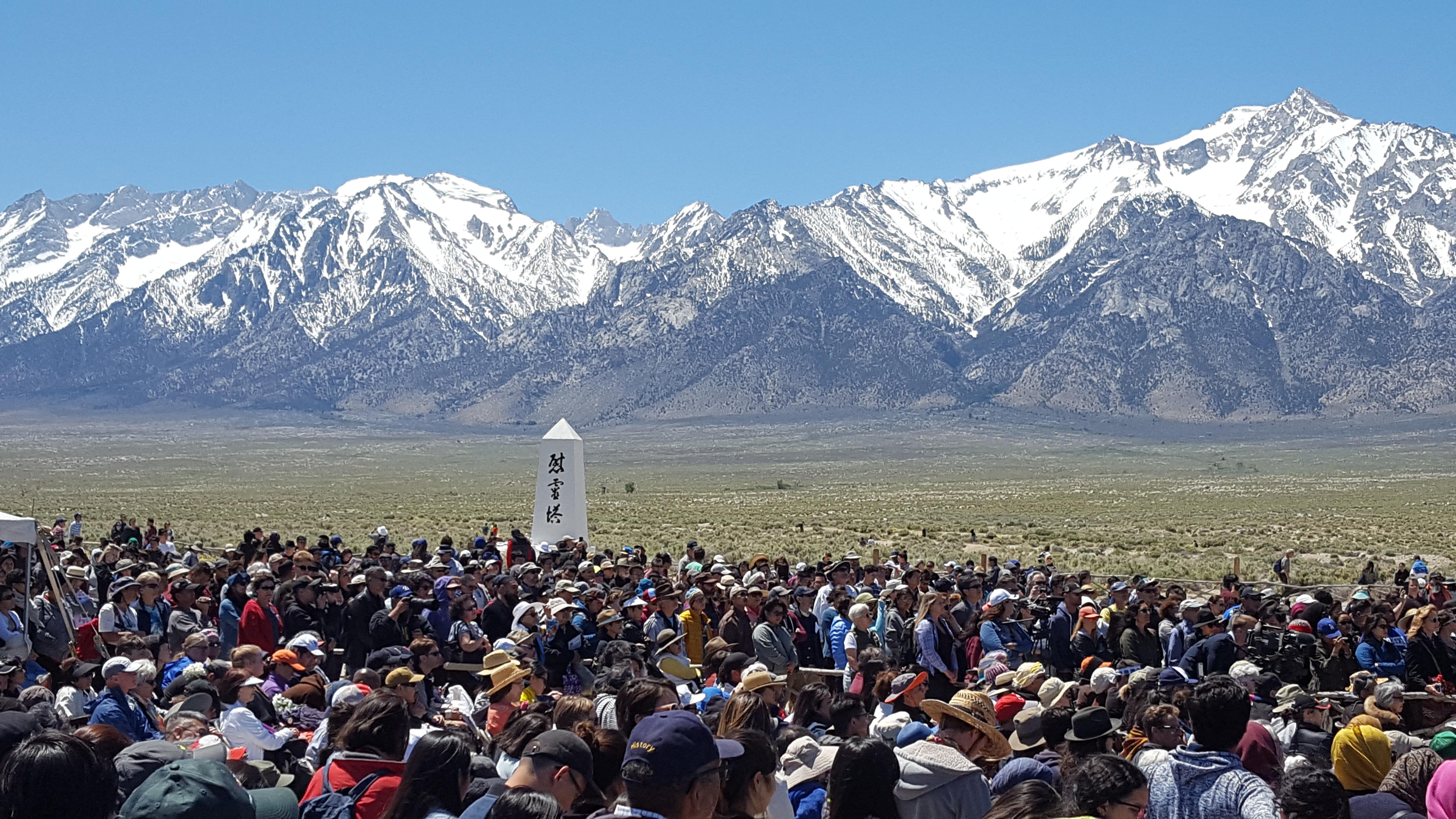 crowd surrounds white obelisk with mountains beyond