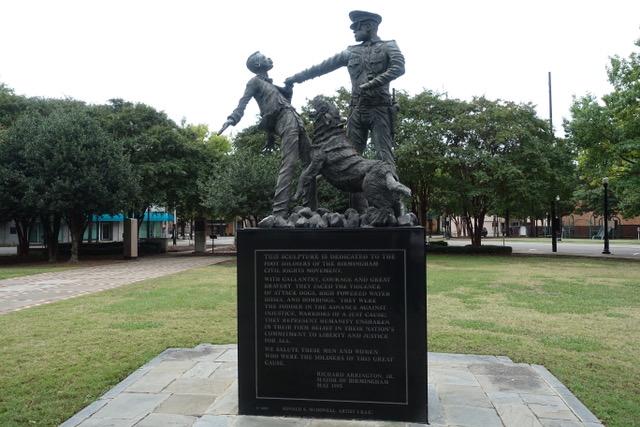 Statue of a boy being grabbed by a policemen who is holding a dog posed to bite on a leash