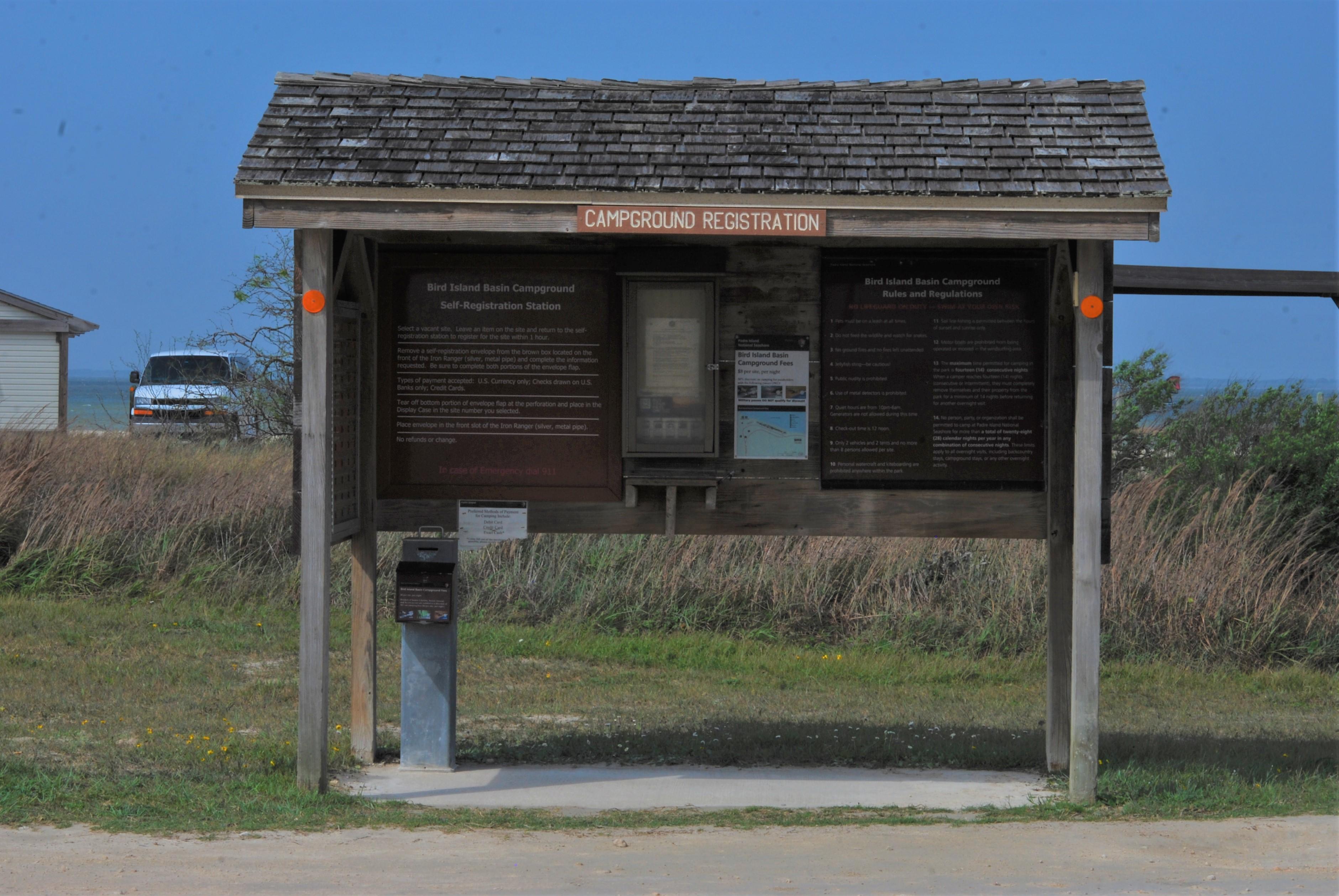 Three-sided rectangular campground registration kiosk over a concrete pad with an iron money drop.