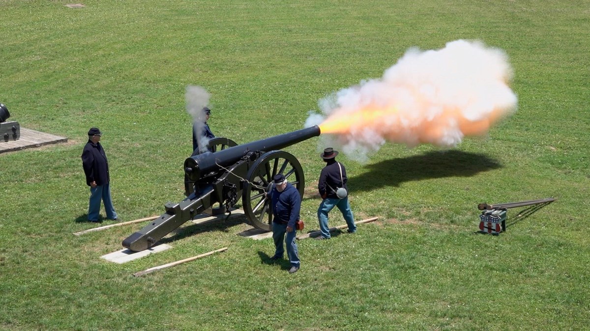 A cannon, surrounded by volunteers in federal uniforms, fires and releases smoke at Fort Pulaski