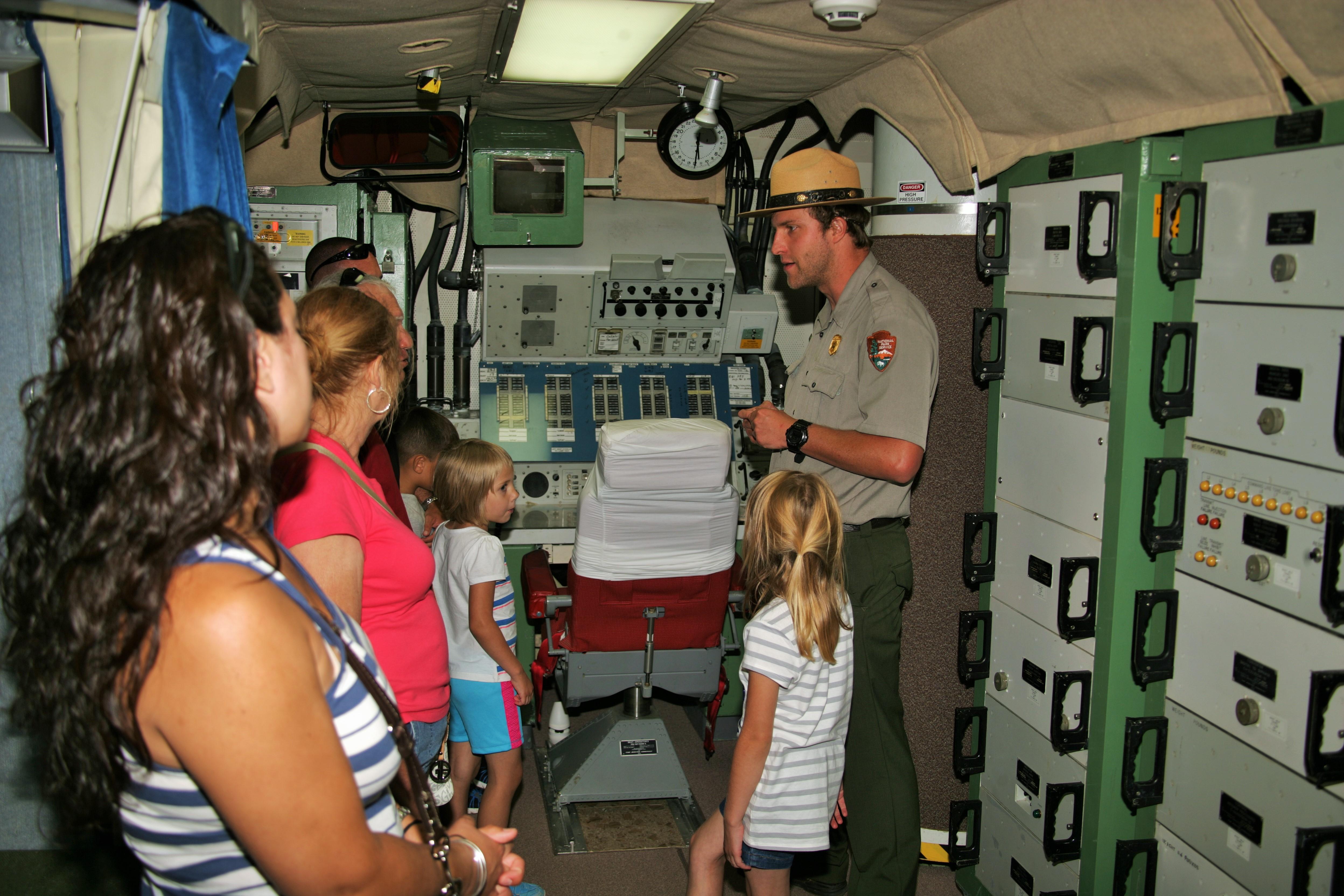 A ranger talks to visitors next to electronic cabinets.