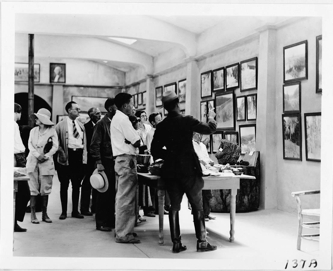A group of people including a male ranger stand inside a museum with walls lined with photos.