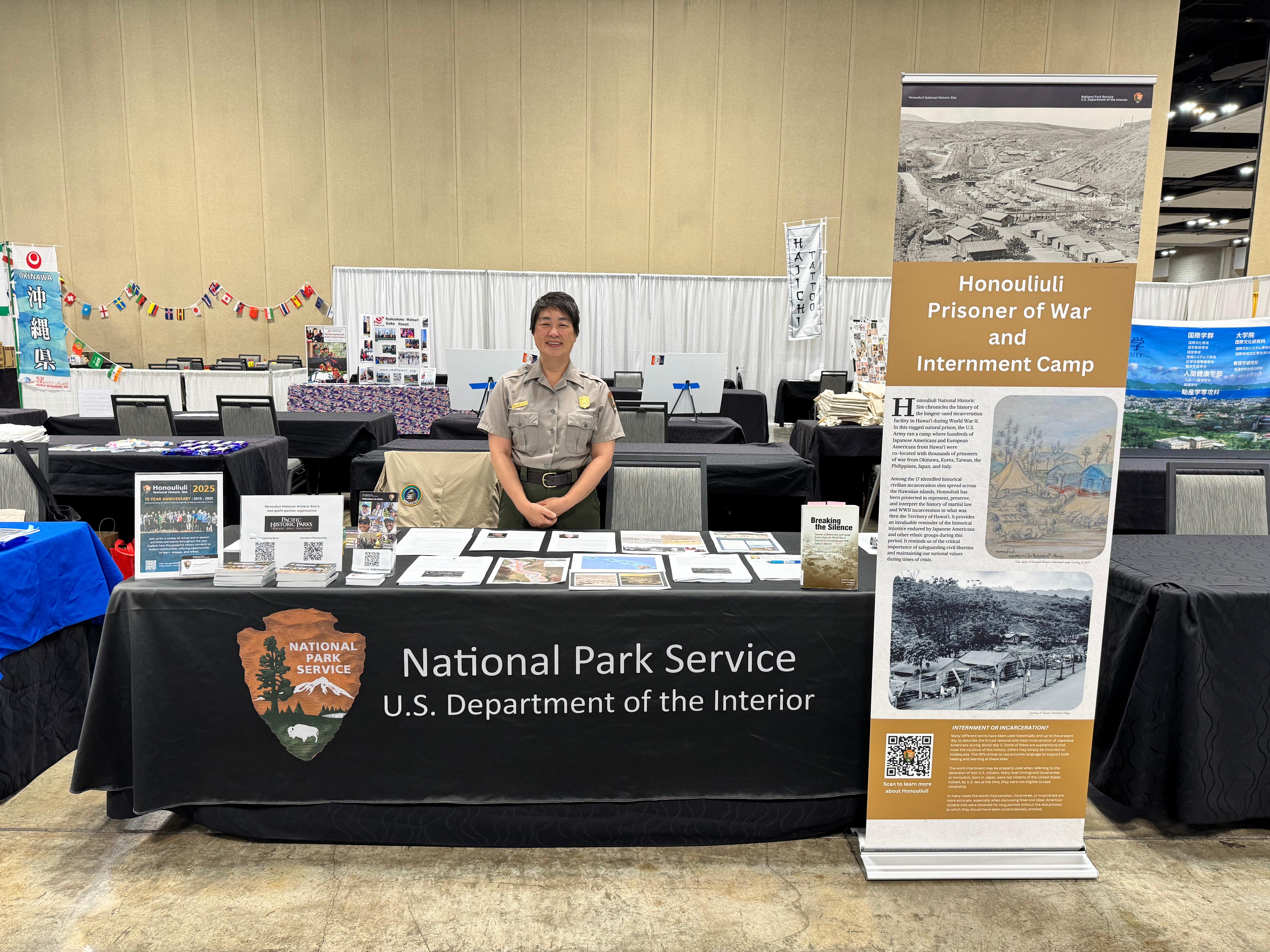 A park ranger stands and smiles behind a booth for the park