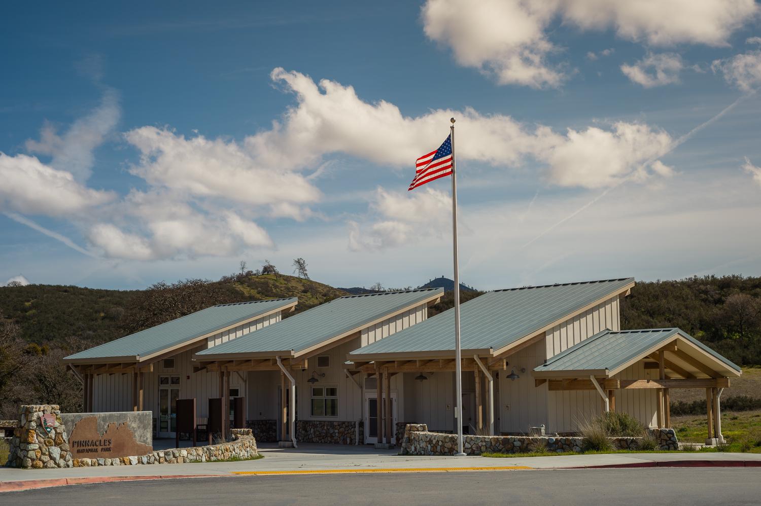 A flag flying next to a welcome visitor center building with three slant roofs