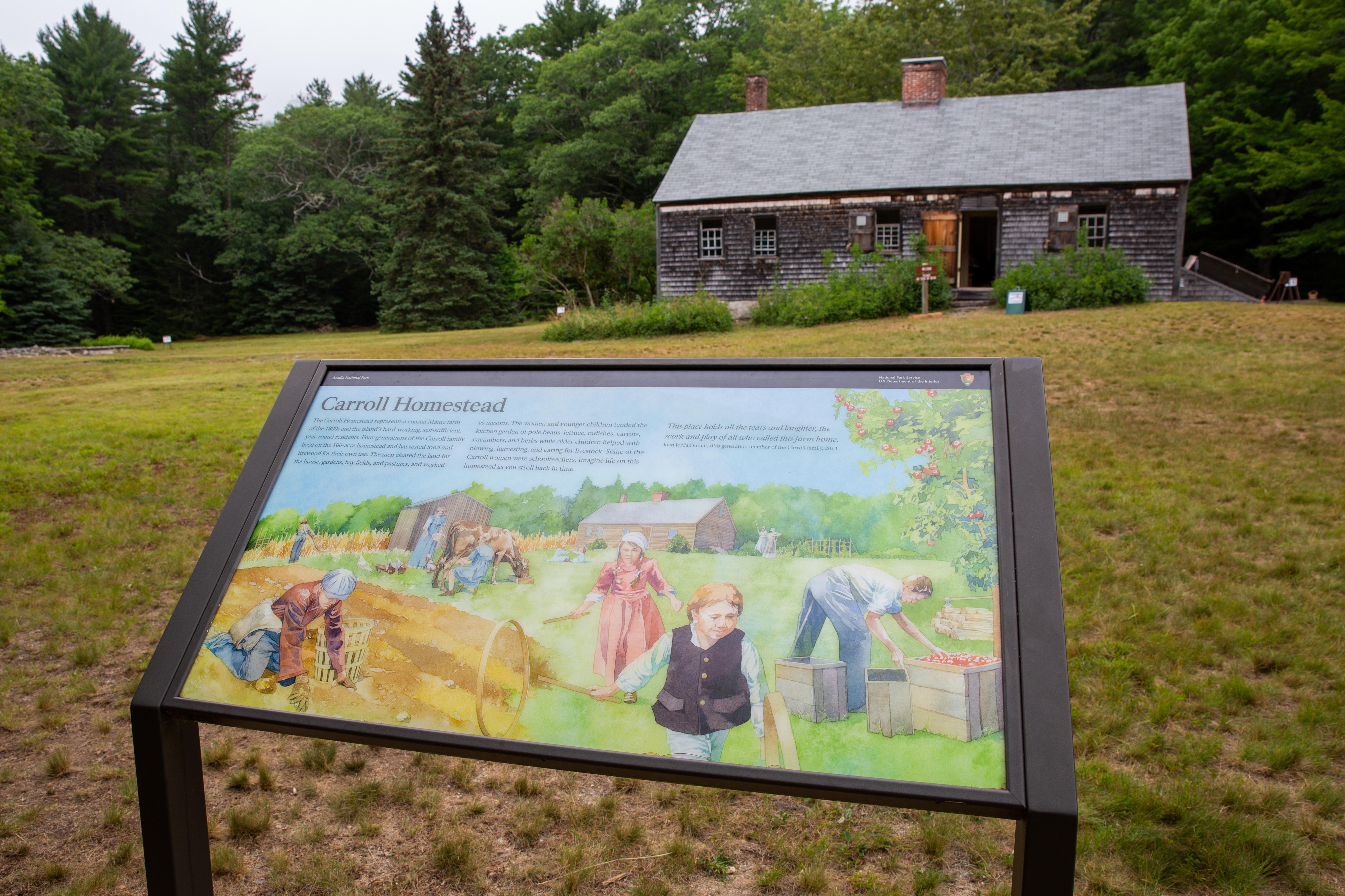 Landscape photo with a small historic farmhouse in the distance and an interpretive wayside in the f