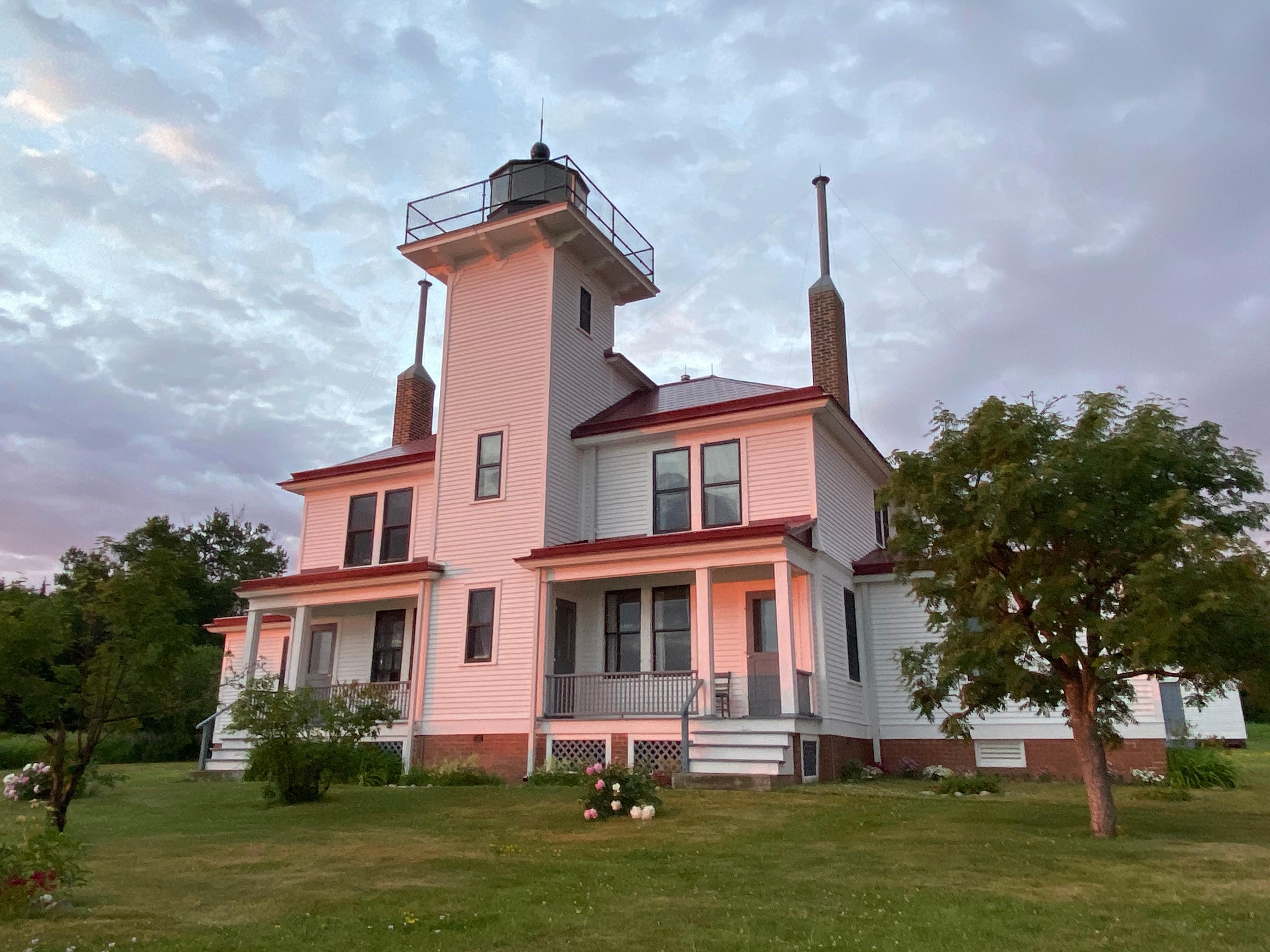 A two story white house with a light tower in the middle, reflects the colors of the setting sun.