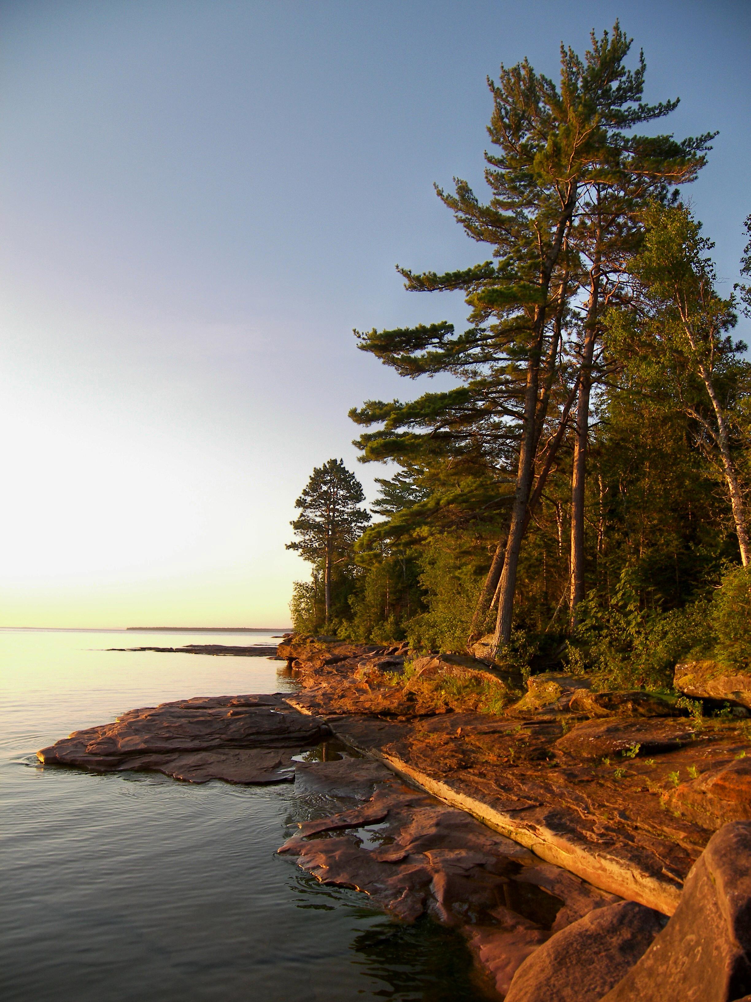 A rocky shoreline meets the calm water of a lake at sunset.