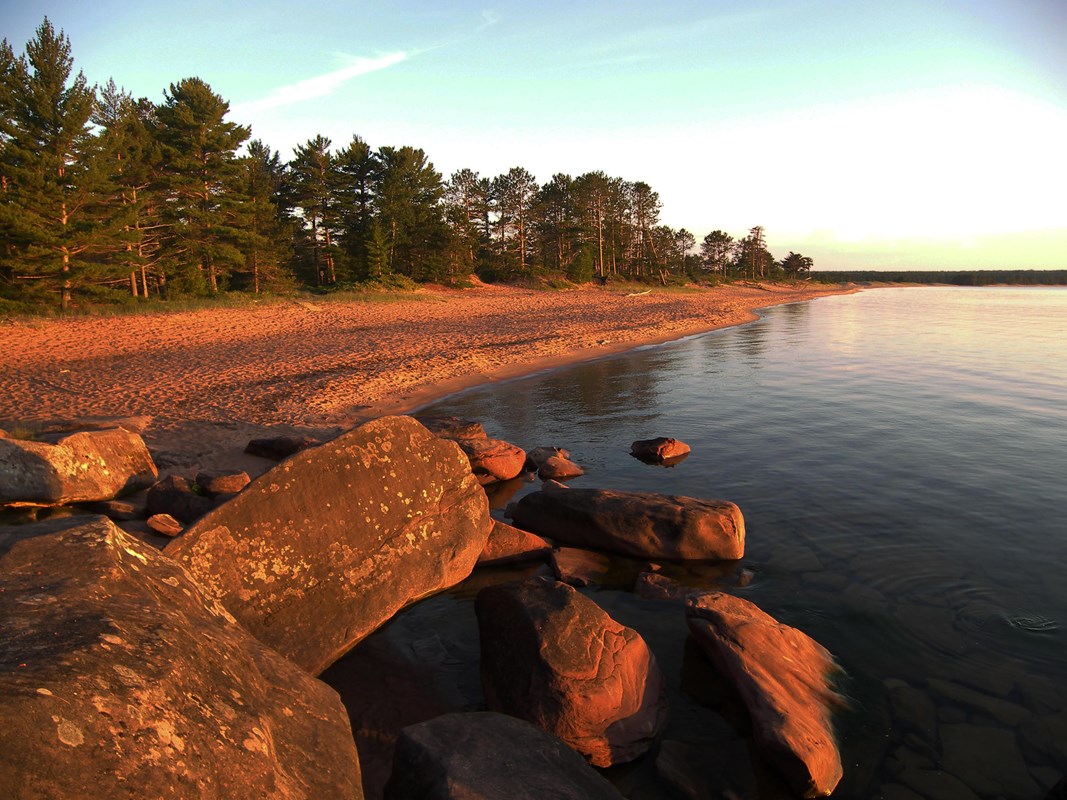 Sunrise illuminates a long beach near calm water. 