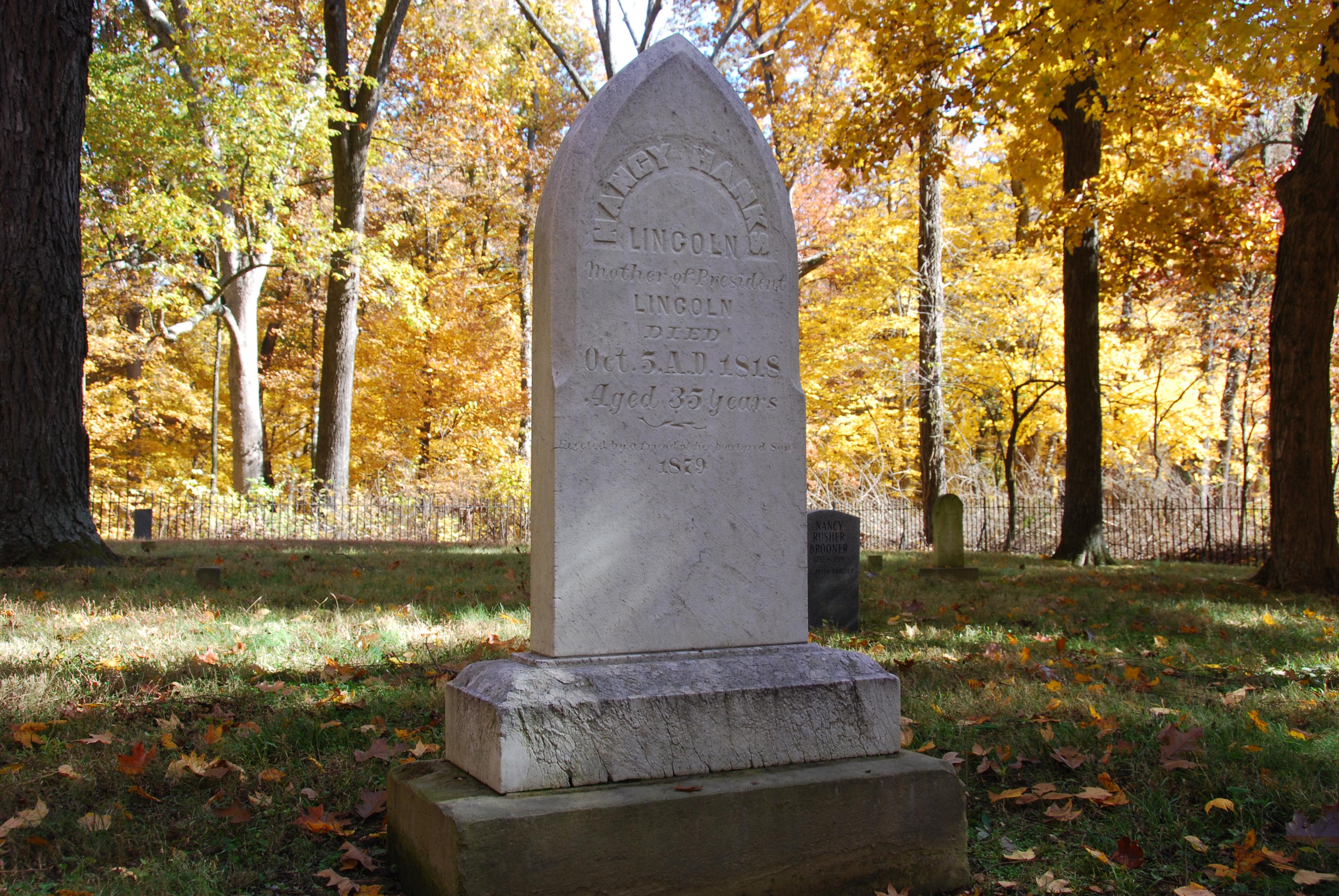 White marble headstone of Nancy Hanks Lincoln in cemetery surrounded by iron fence and trees.