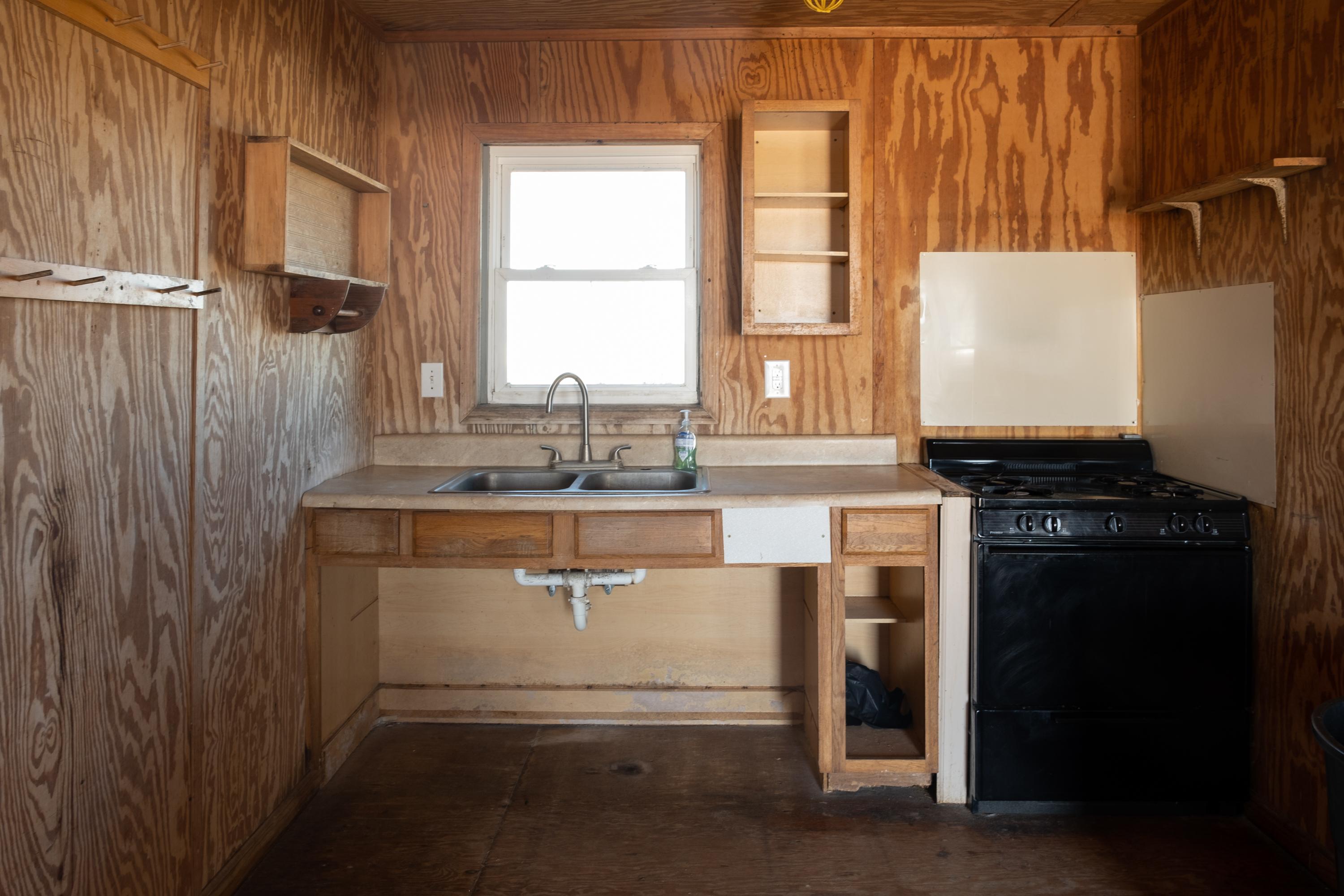 A sink next to a stove. A window above the sink