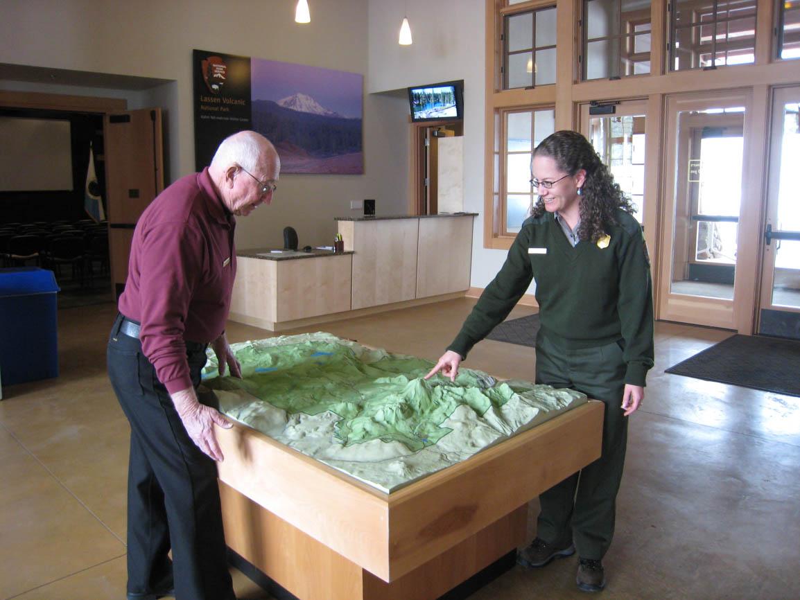 A woman in a uniform and a man stand at a 3D map inside a visitor center.