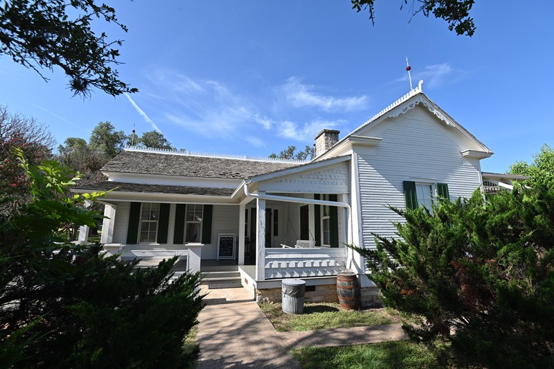 Lyndon Johnson Boyhood Home A one-story white frame house with green shutters stands against a brilliant blue sky.