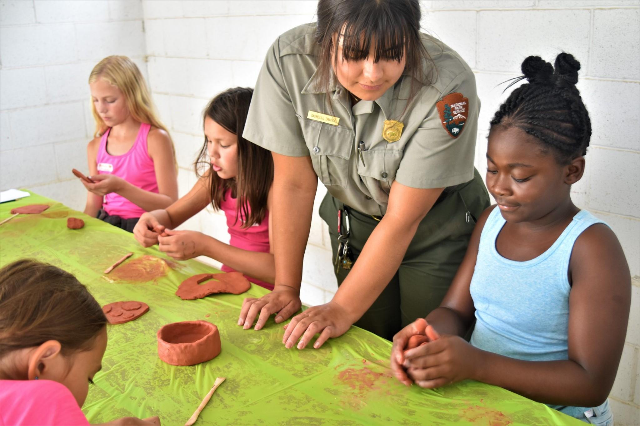 A woman standing next to a little girl helping her make a clay pot