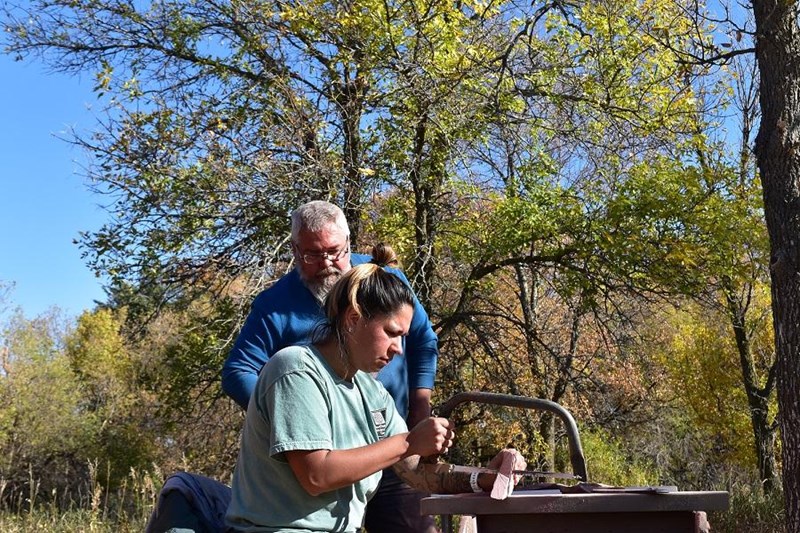 Learning to Carve Pipestone A man watches over a woman as she saws a piece of stone