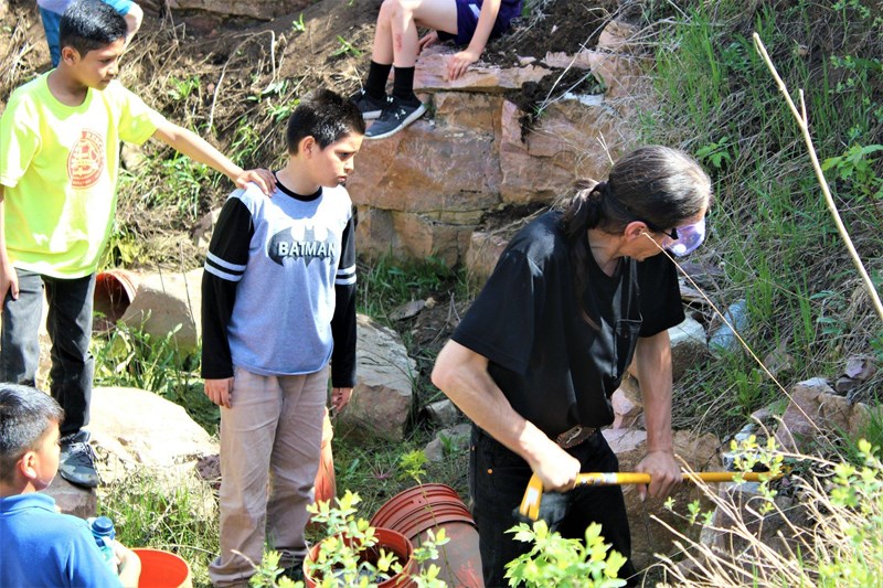 Teaching the Next Generation A man works with tools in a quarry as kids watch