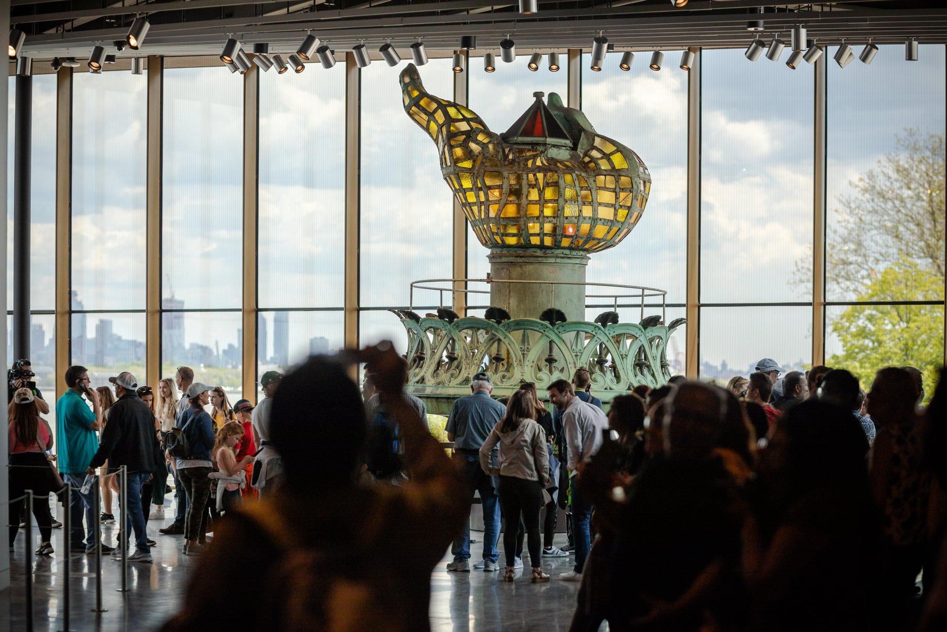 A room is filled with people with the original torch on display in the background.