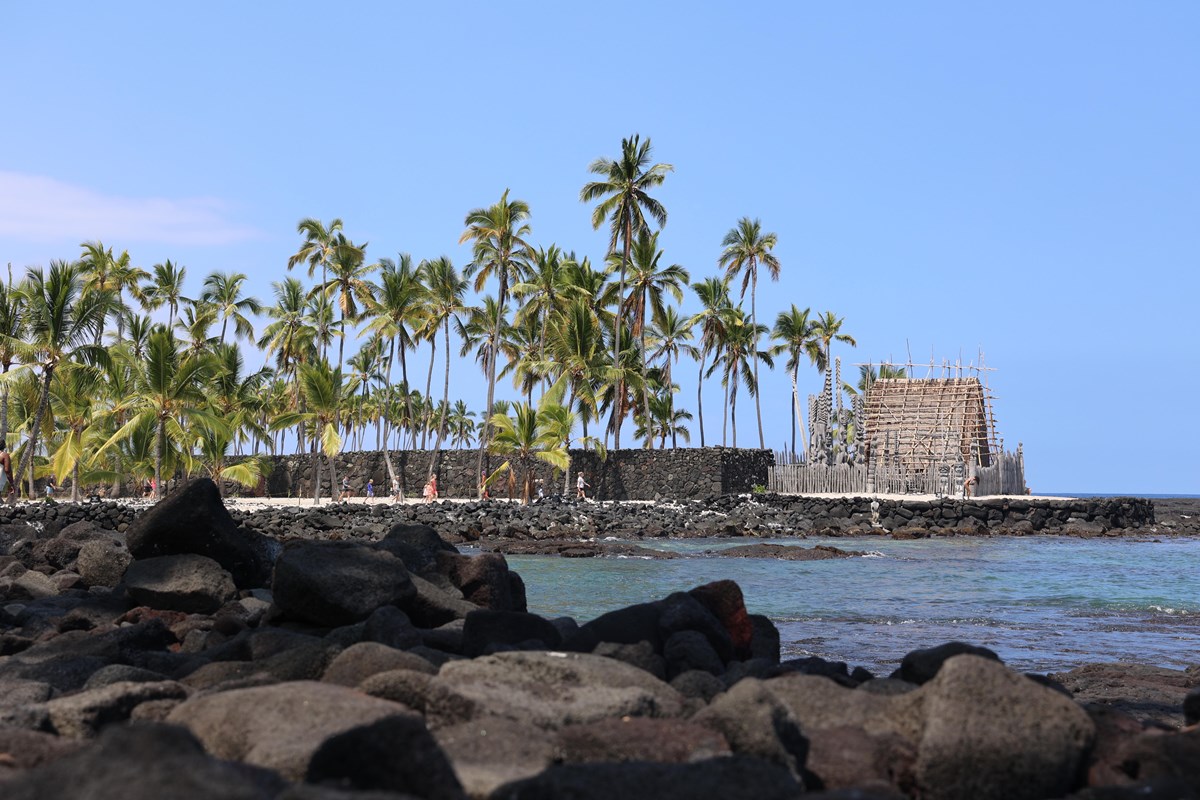 Sacred temple and coconut trees next to the ocean as viewed from a rocky wall across the bay.
